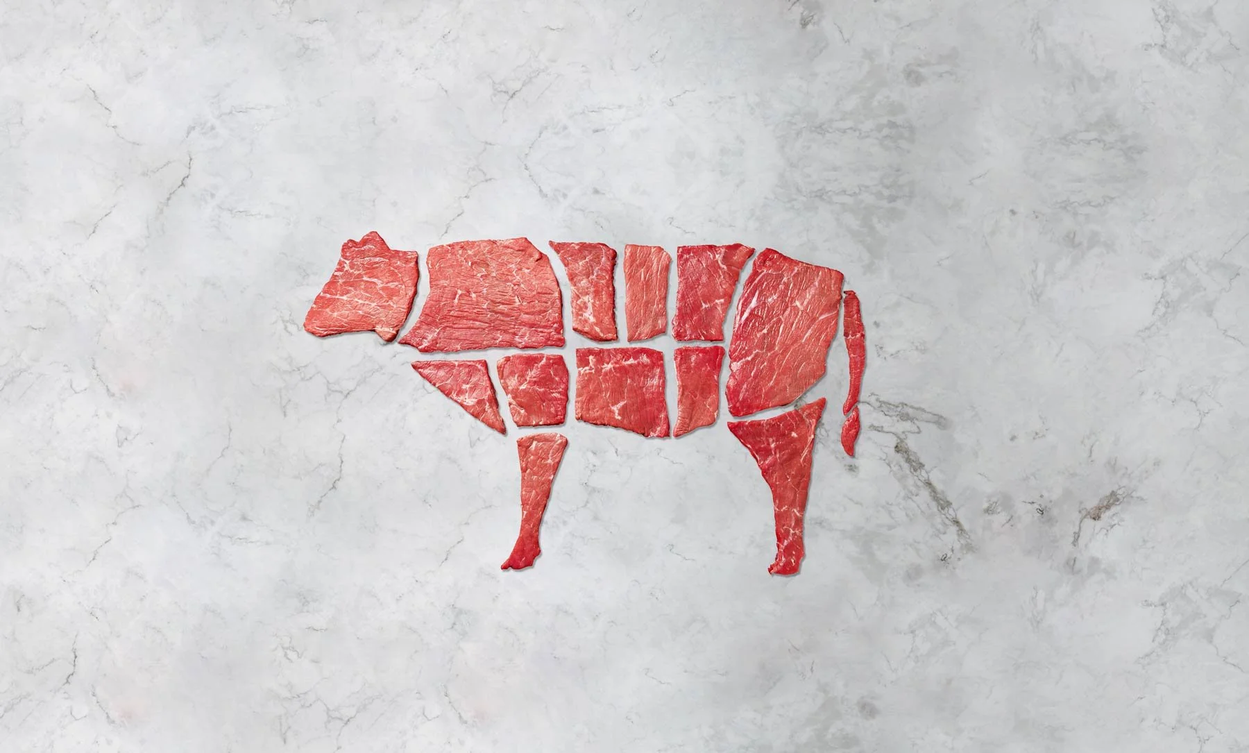 Pieces of raw beef arranged to form the shape of a bull on a gray marble surface.