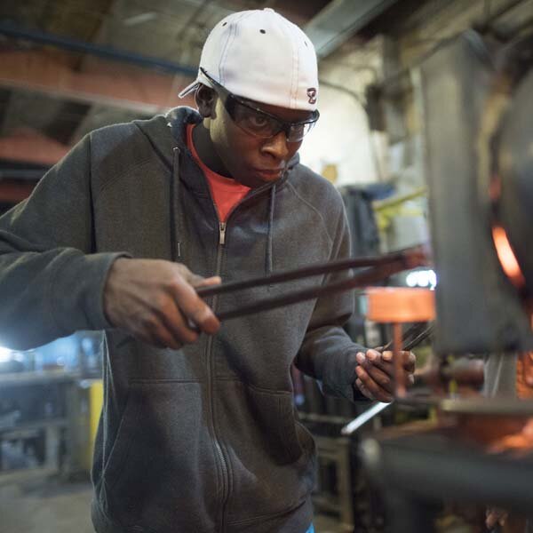  Photo of blacksmithing student putting metal into the forge. 