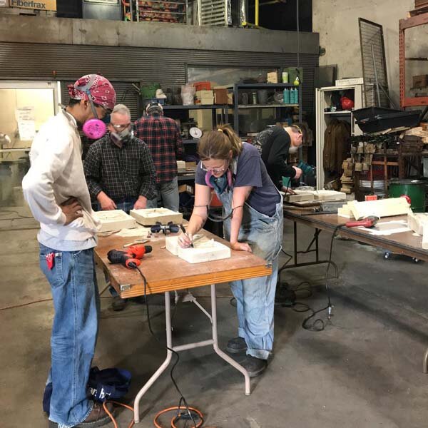  Photo of casting artist teaching students how to make sand molds. 