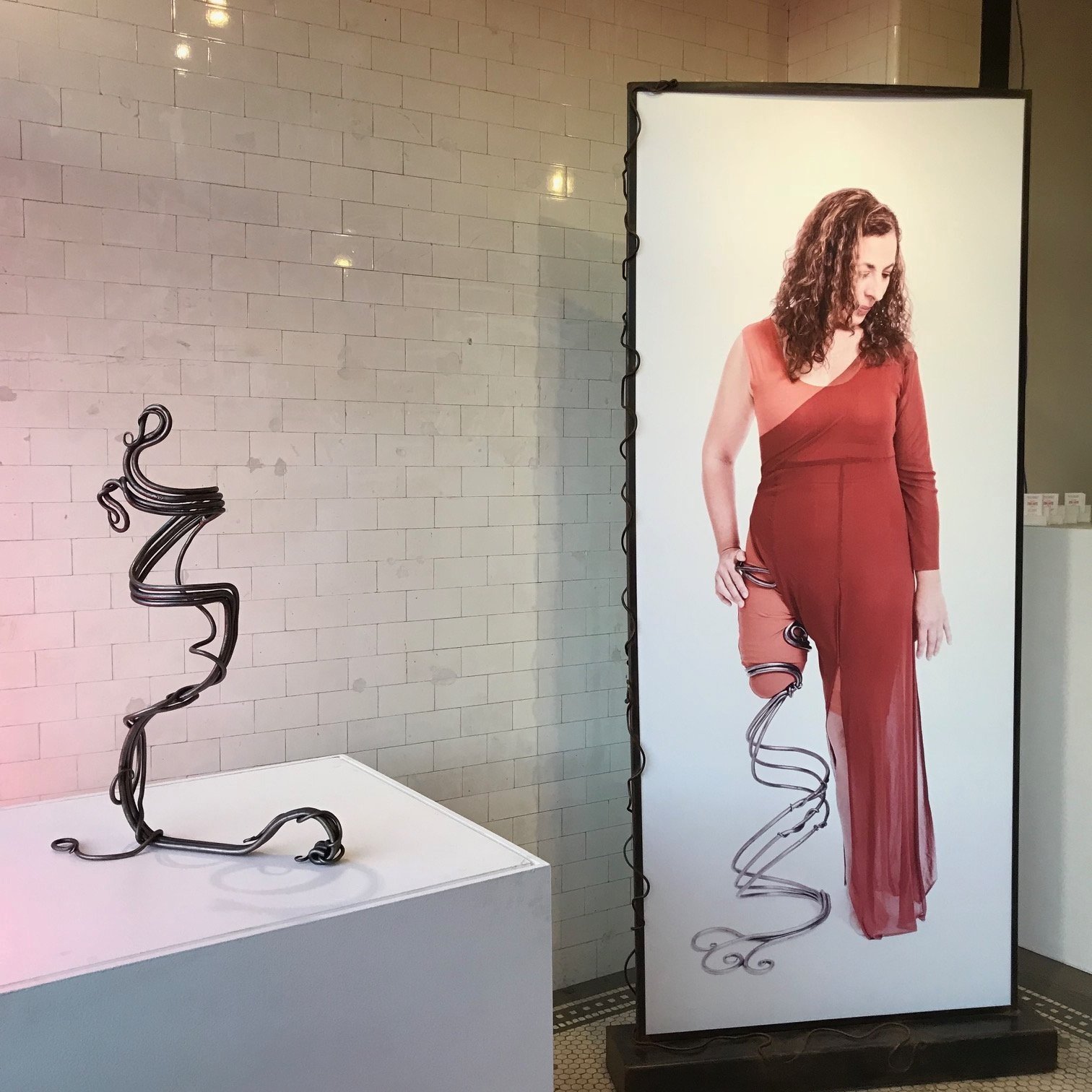 Photo of a curvilinear sculpture on a pedestal and a lifesized photograph next to it.