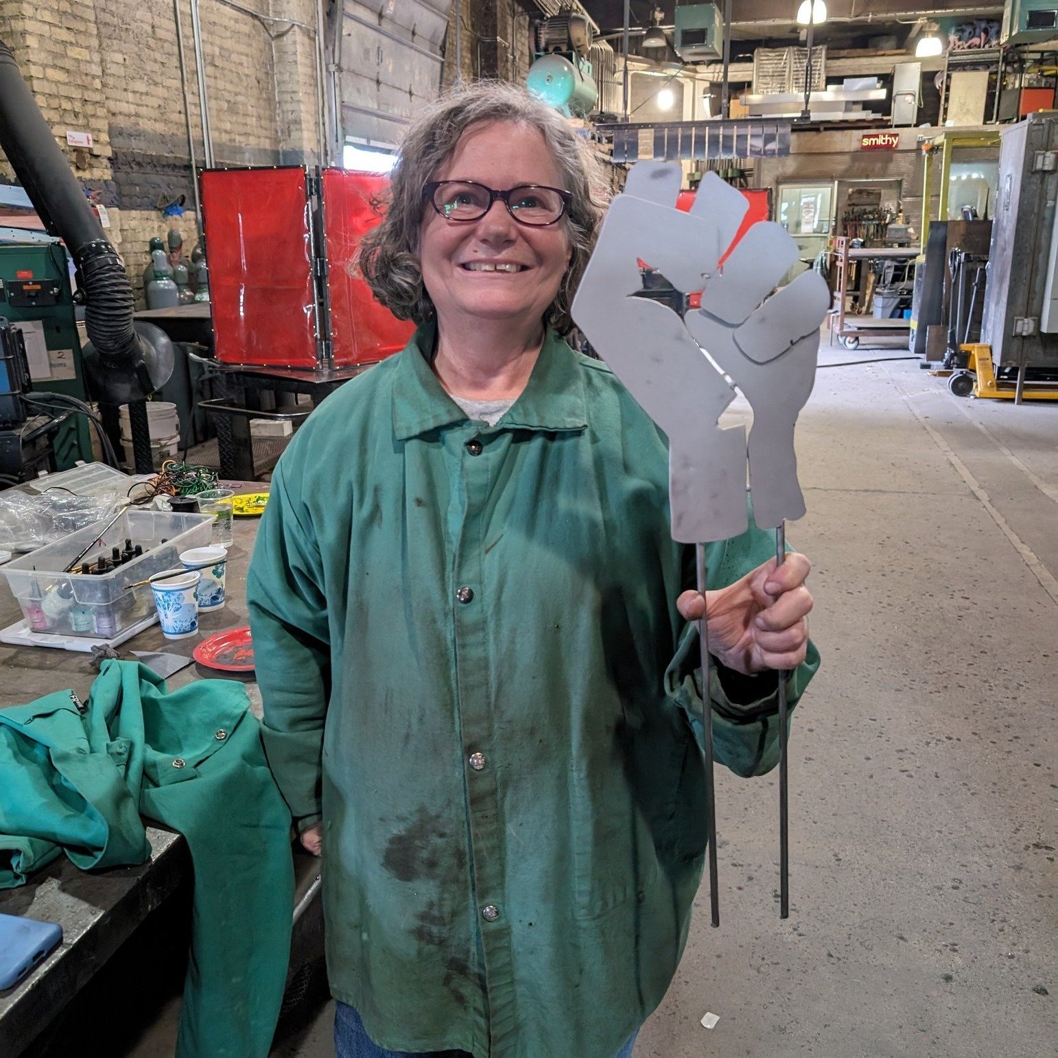 Today's GFS neighbor workshop was a success! We saw one garden stake fist and a whole bunch of cast pewter fist pendants and pins made by participants. More to come in June!

[Image descriptions: 1. A woman stands smiling at the camera, holding up he