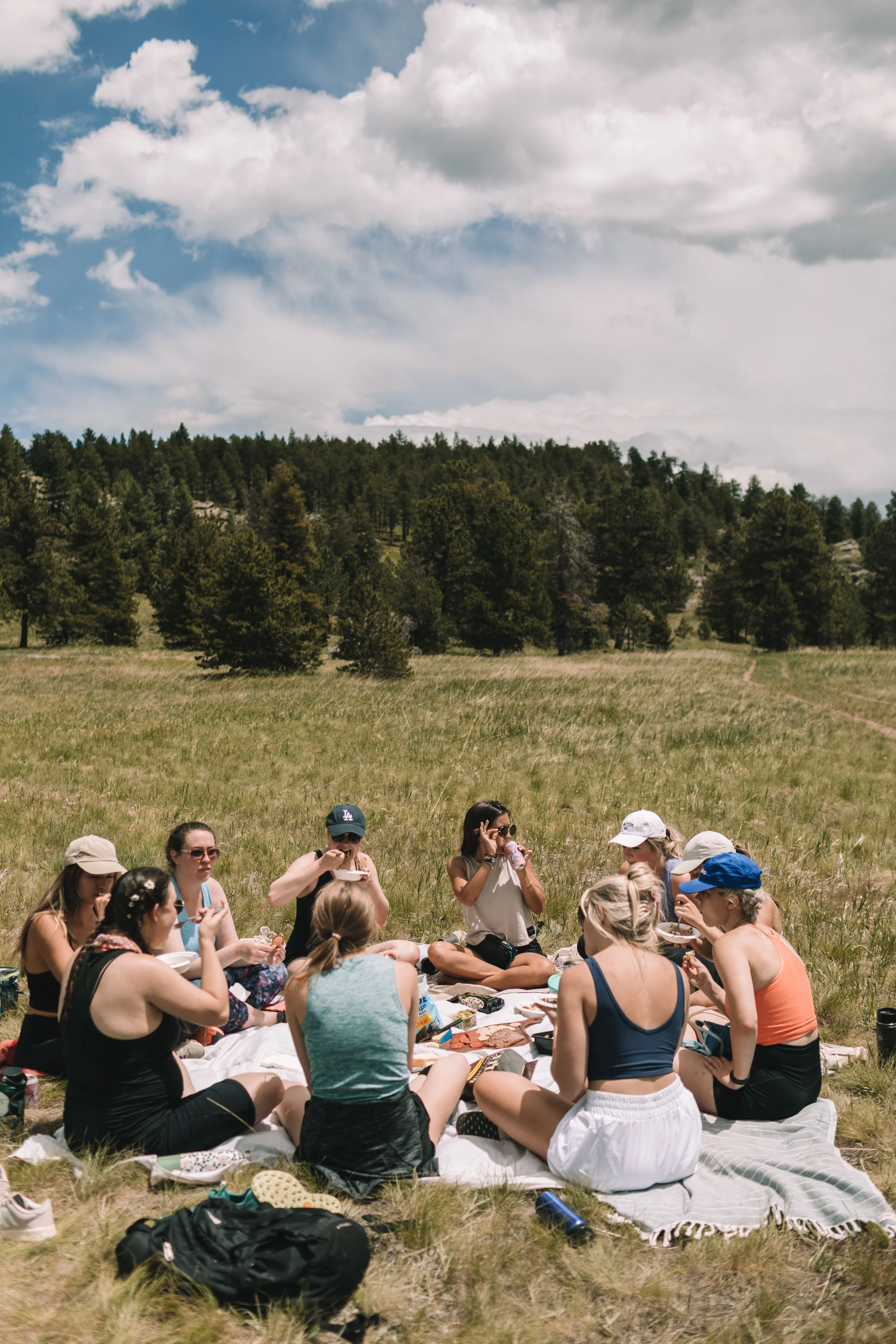 a group of young women enjoy a picnic meal outside with blue skies and wispy clouds in the background