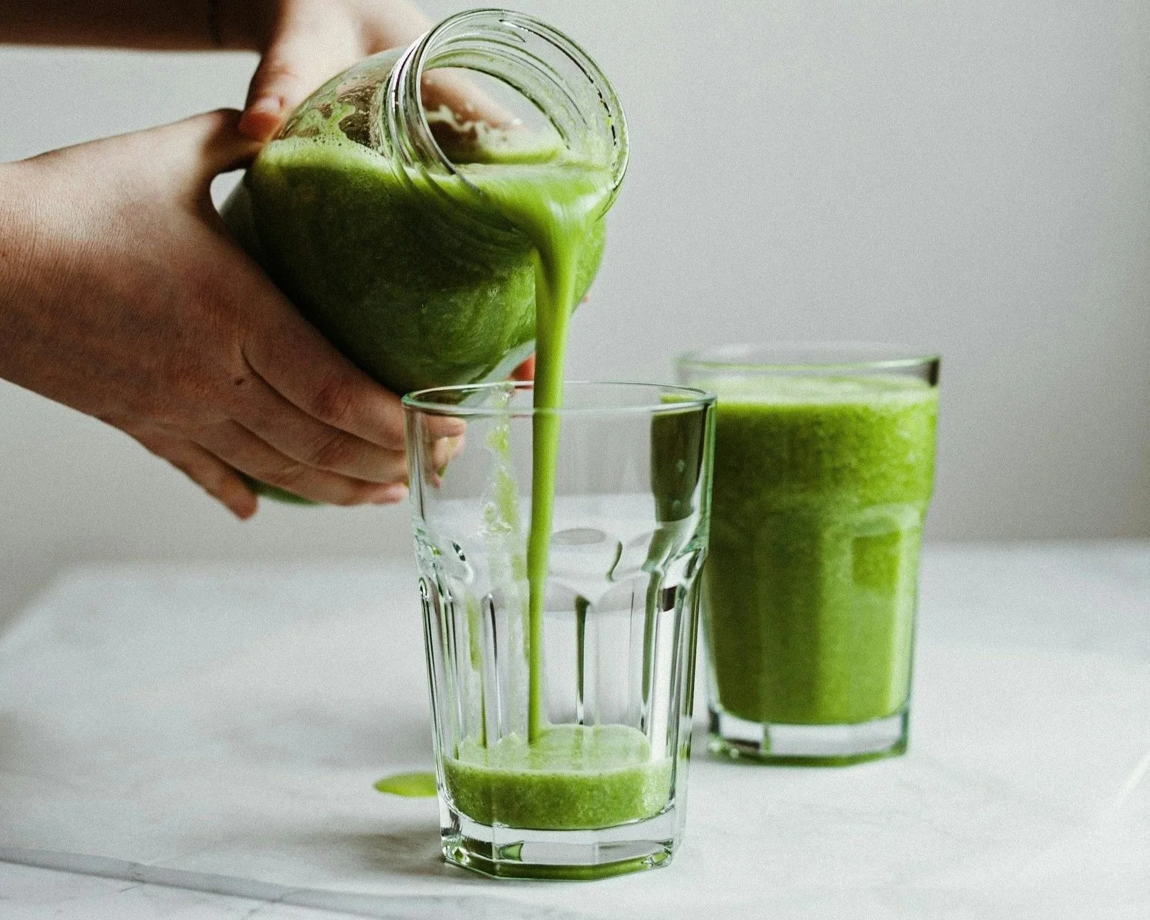 a green smoothie mixture being poured into a clear drinking glass