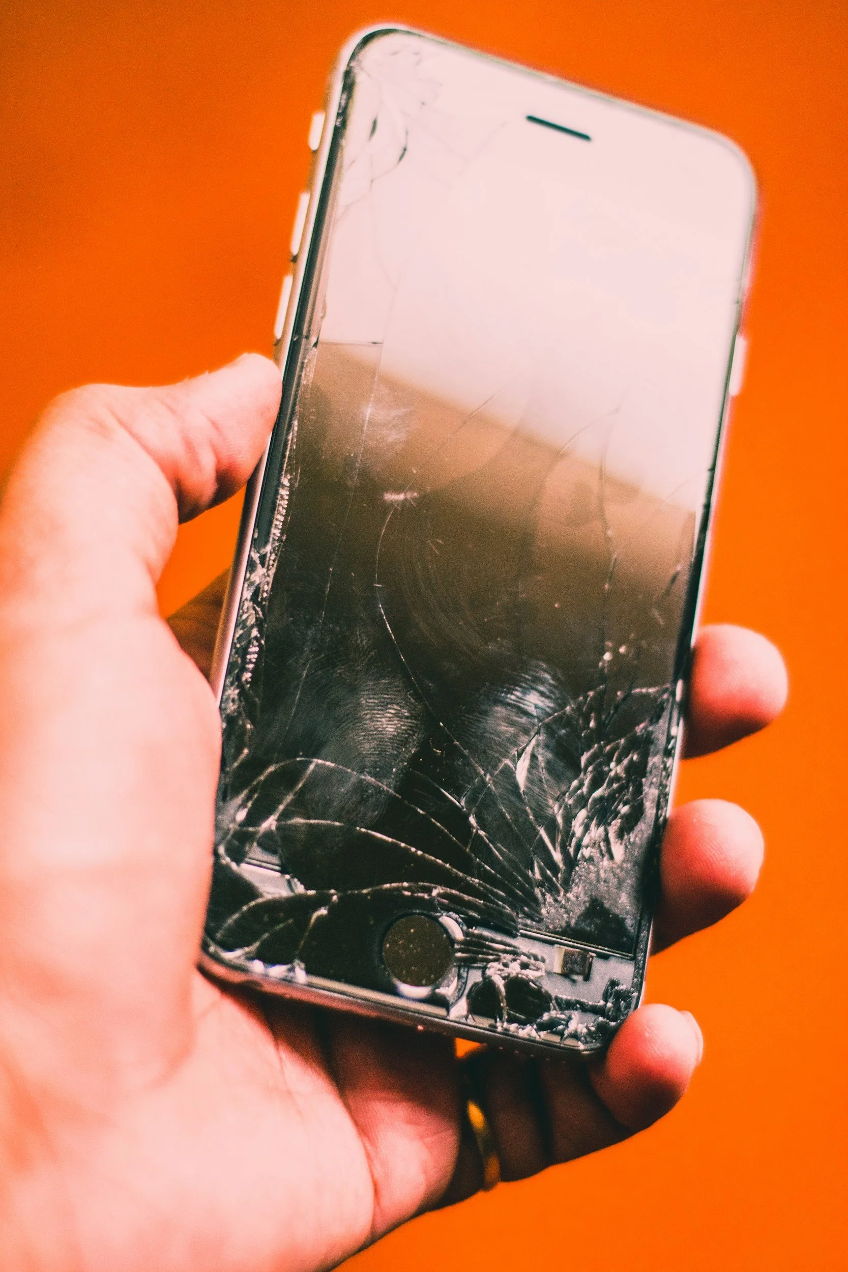 Hand holding phone showing cracked screen, representing trickle truth and repeated disclosures in betrayal trauma