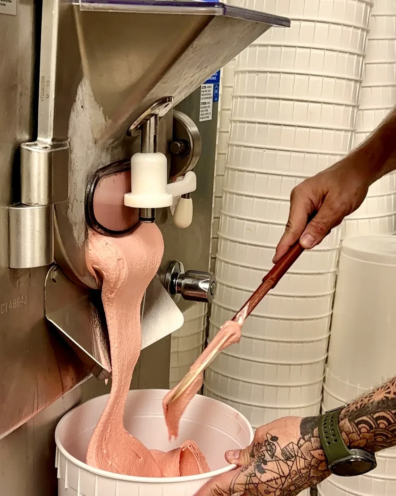 Fresh strawberry ice cream flowing out of the machine into a tub