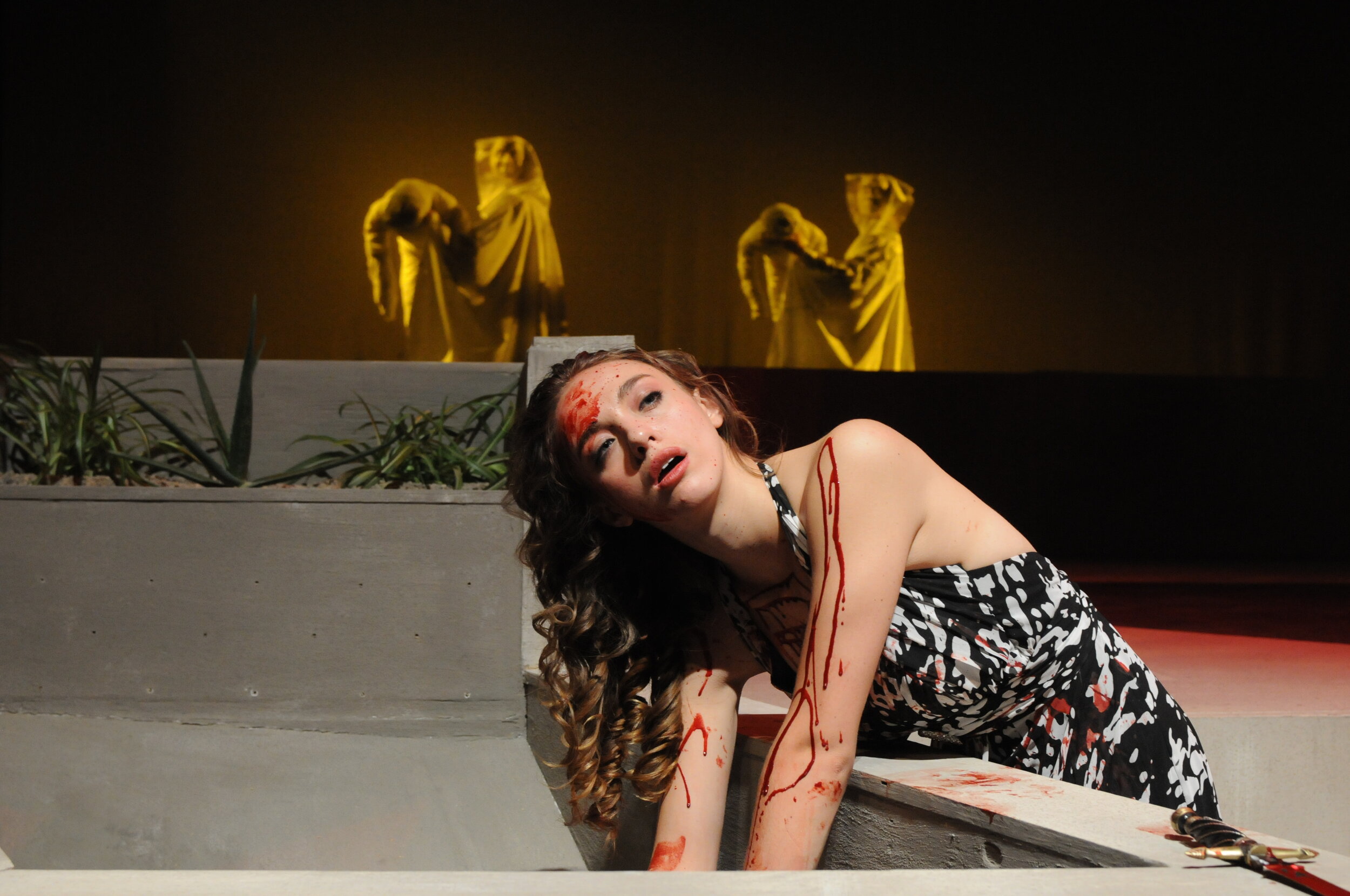   Bodies of Medea’s dead children are carried across stage as she washes off their blood  