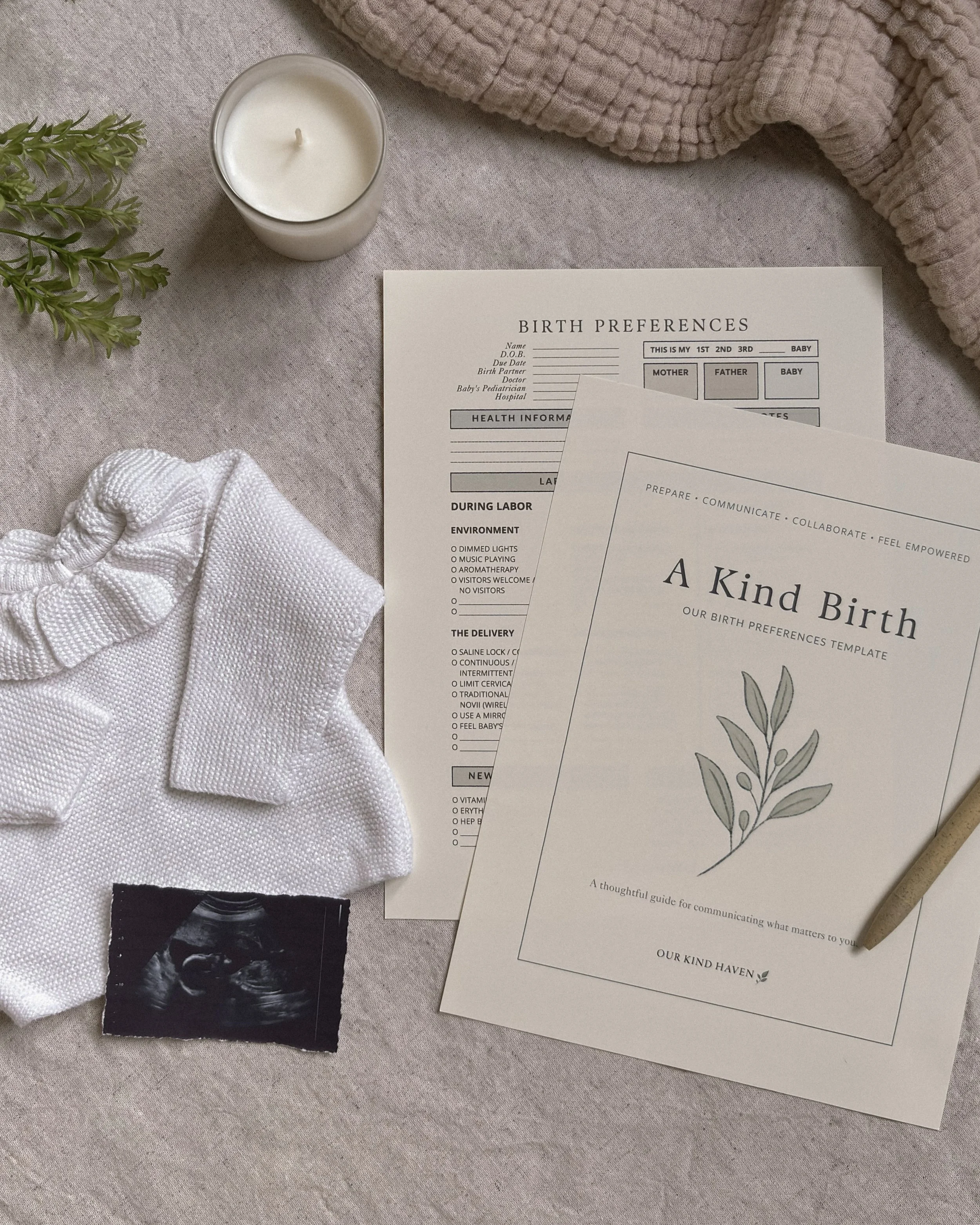 Flat lay of A Kind Birth printable birth plan alongside a baby outfit, ultrasound photo, swaddle, candle, greenery, and pen on a soft linen backdrop.