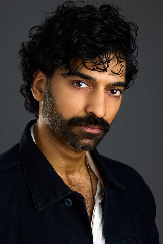 Professional headshot of a man with curly dark hair and a beard against a dark background