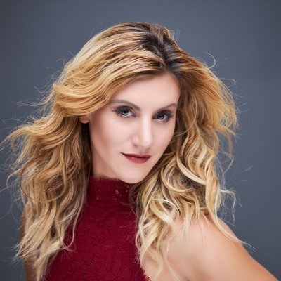 Professional headshot of a smiling woman with long blonde hair in a red top against a gray background