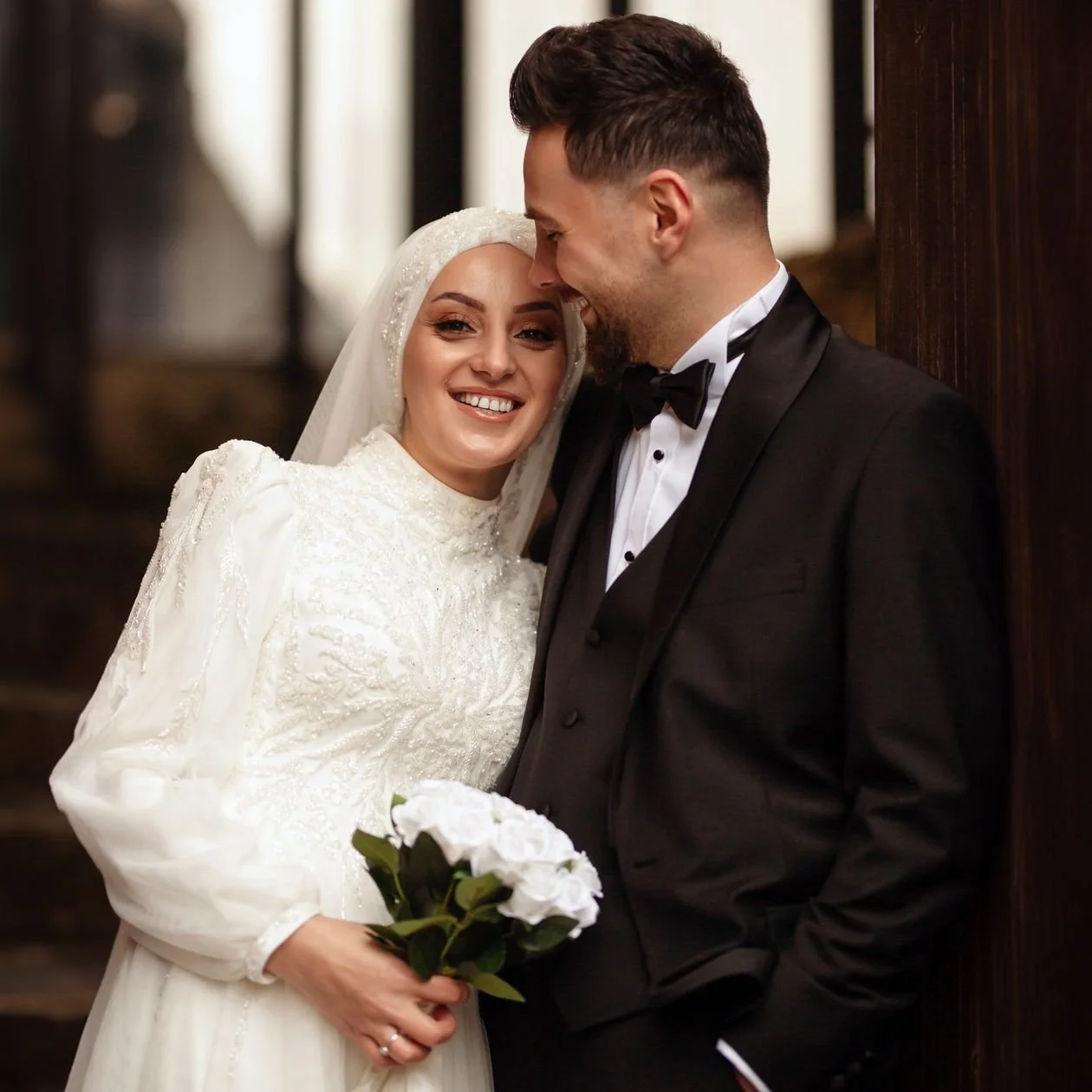 Smiling bride in a white gown and veil holding white roses beside a groom in a black tuxedo, the classic portrait every Los Angeles engagement photo session builds toward