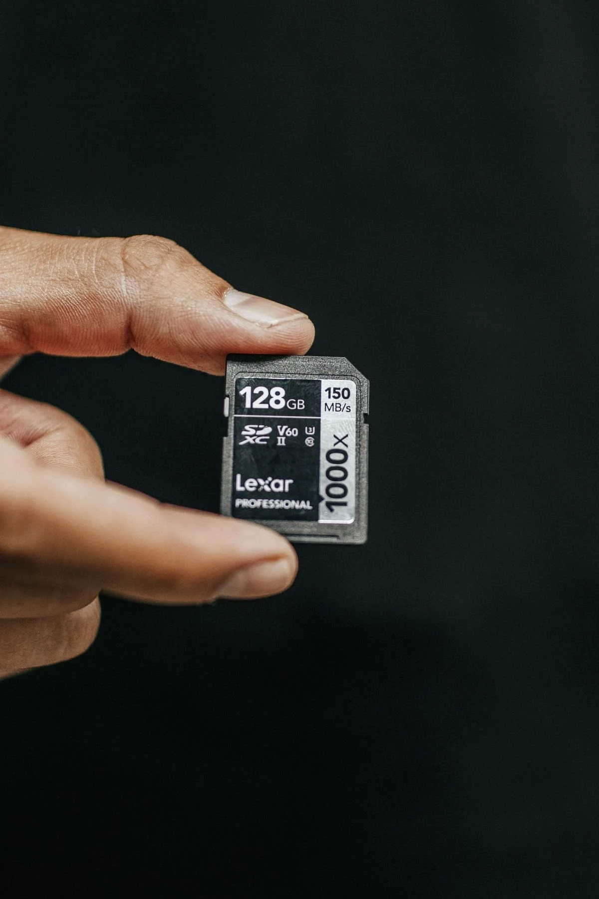 Hand holding a 128GB SD memory card, the first link in a photography backup workflow.