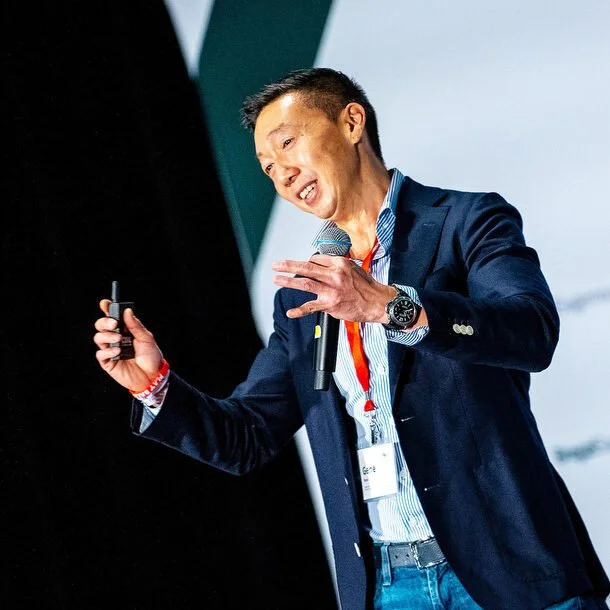 Business speaker presenting on stage at a corporate conference, holding a microphone and presentation clicker, wearing a blazer and a conference badge