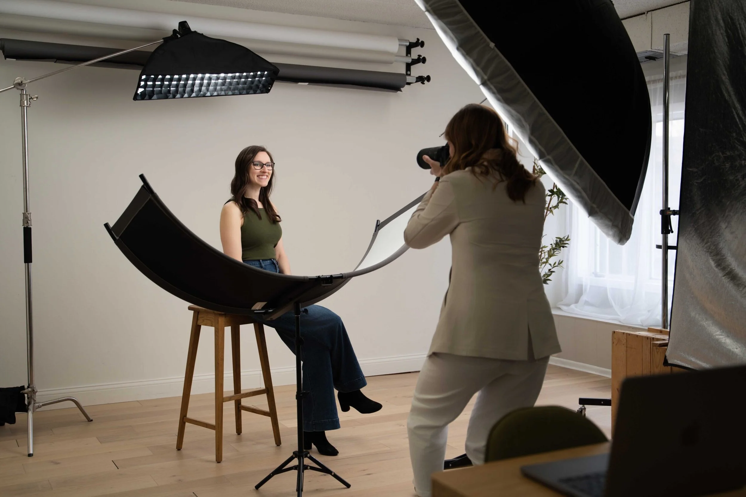 Behind the scenes of a studio headshot session with a photographer shooting a seated woman under a gridded softbox