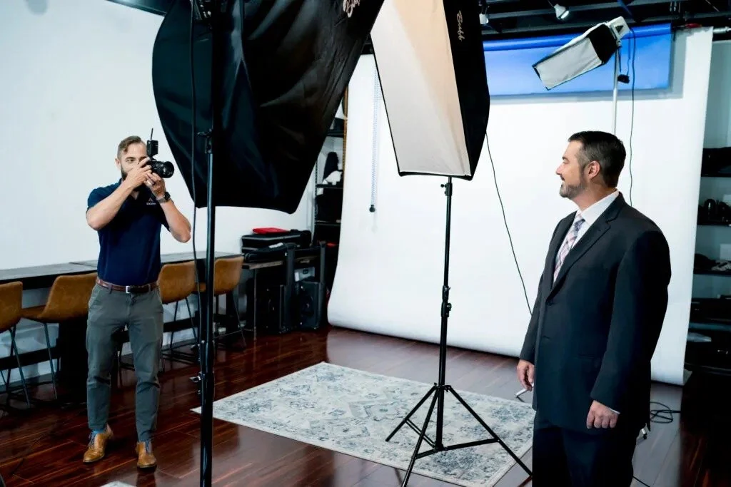 Photographer shooting a businessman in a suit against a white backdrop with two studio softboxes during a headshot session