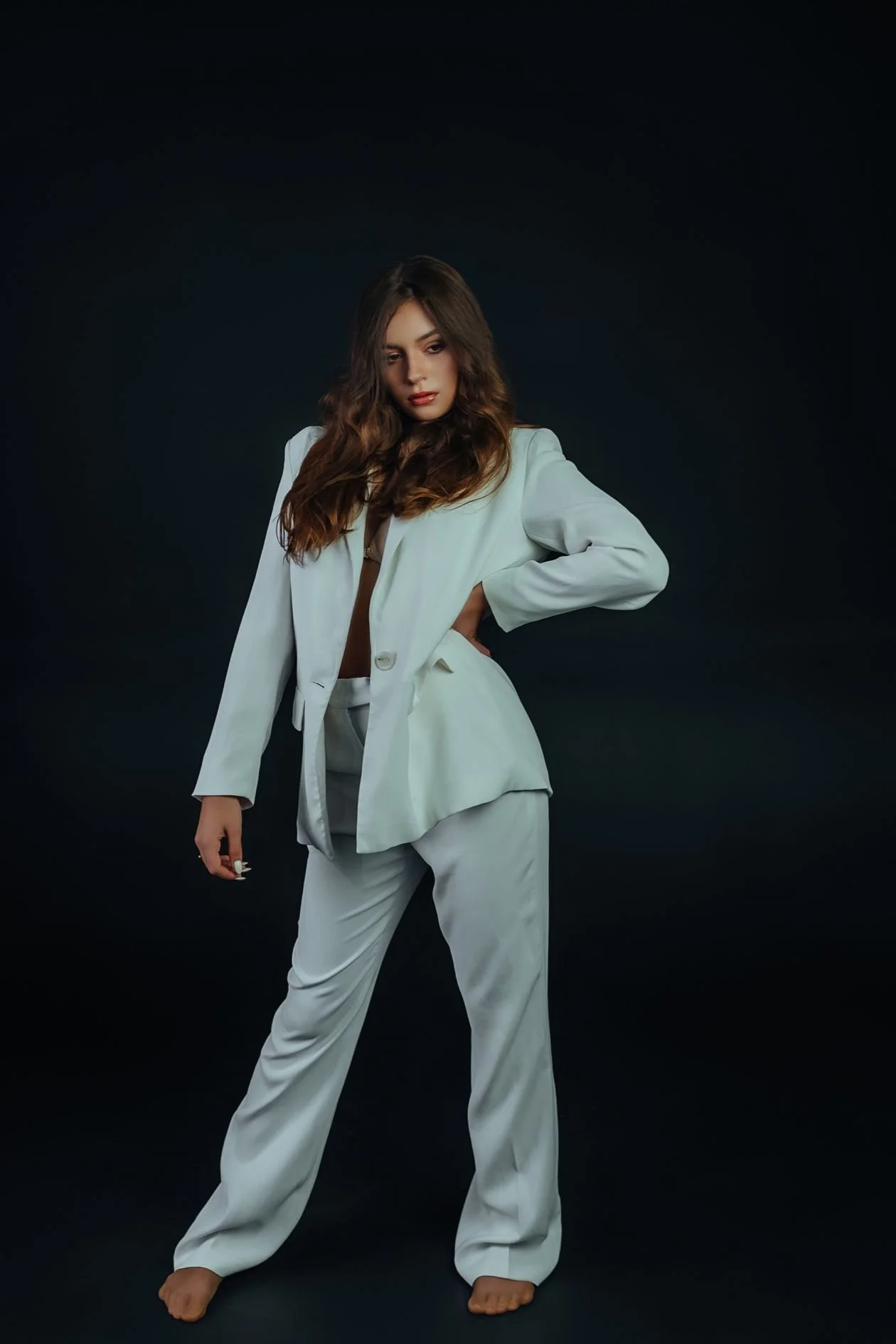 Fashion model in a cream suit holding a directed full-length pose against a dark studio backdrop