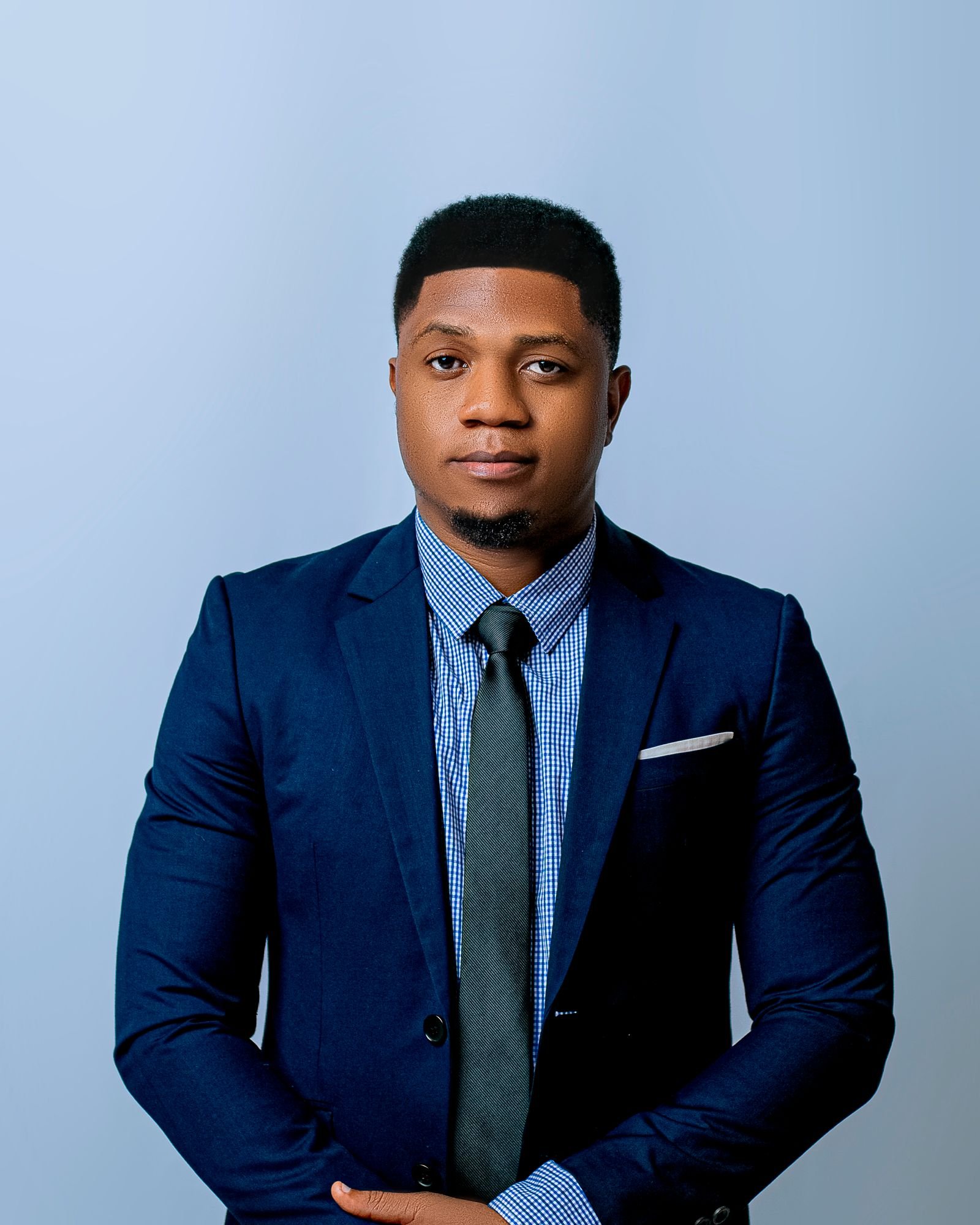 Studio portrait of a confident man in a navy suit, checked shirt, and dark tie against a light gray background
