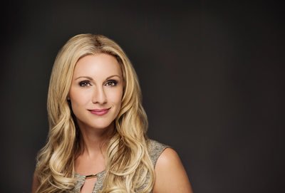 Professional headshot of a smiling blonde woman against a dark background