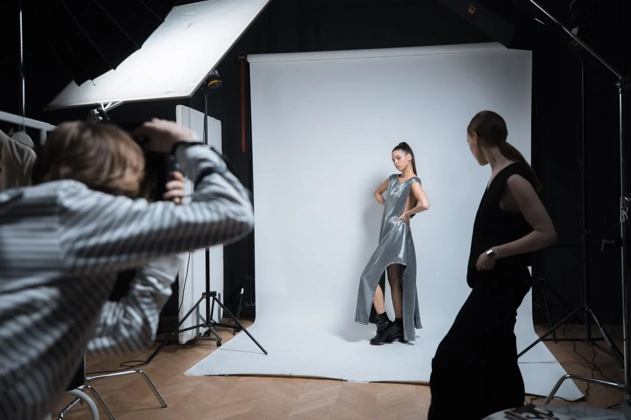 Fashion photographer in Los Angeles shooting a model in a metallic dress on a studio set while a stylist watches