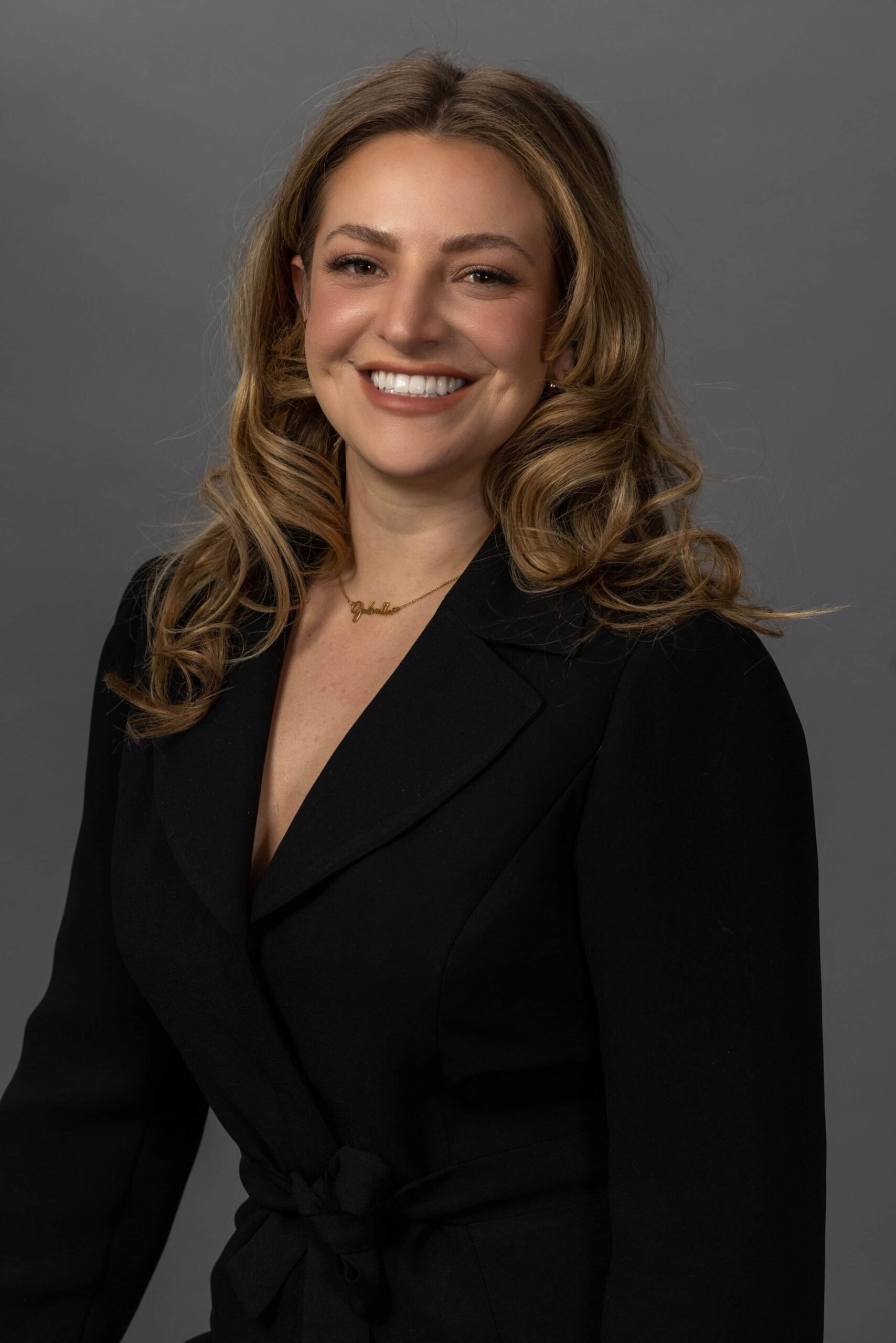 Studio headshot of a smiling woman with wavy brown hair against a gray backdrop
