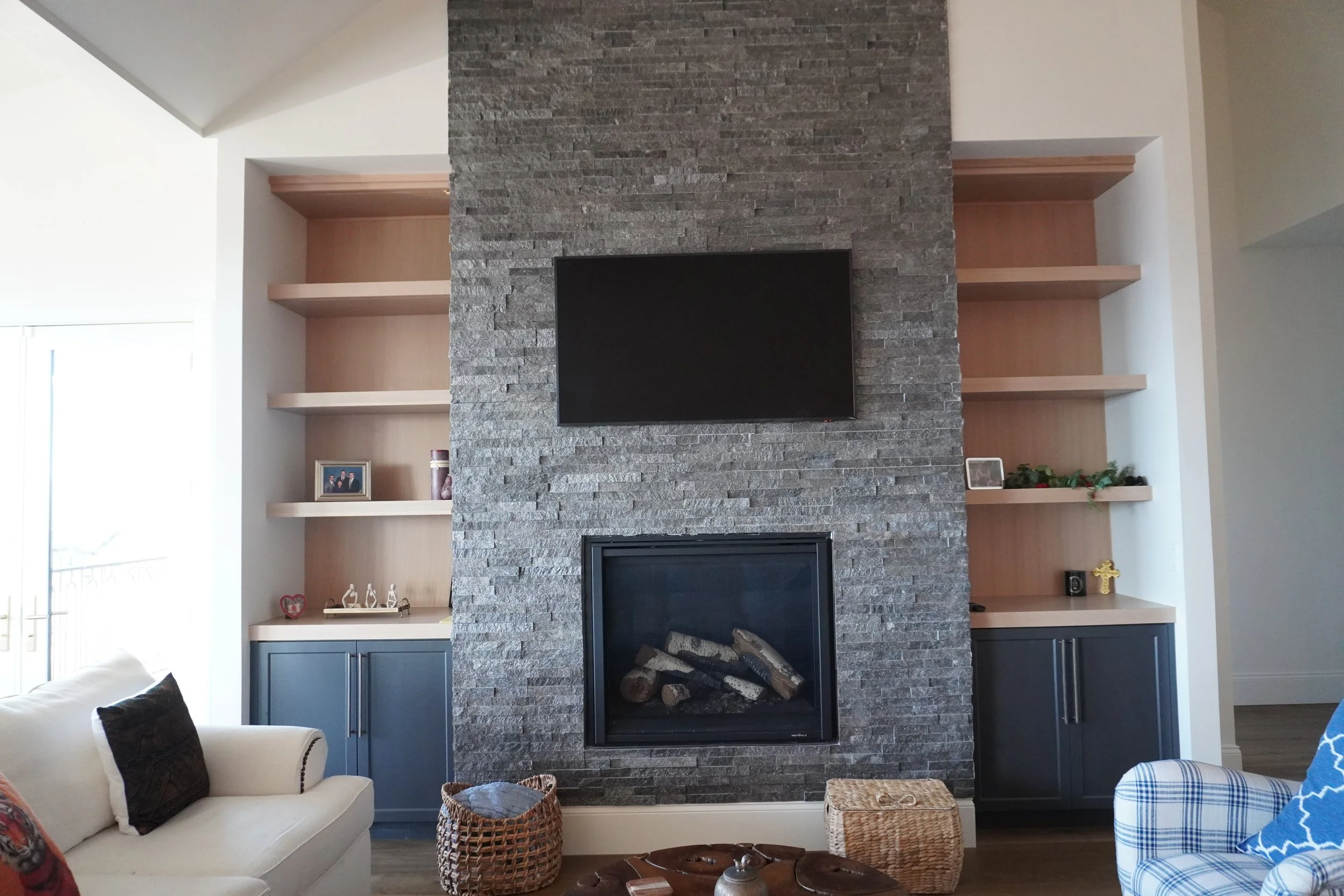 Living room with a stone fireplace, mounted television above it, and built-in shelves with decorative items on both sides.