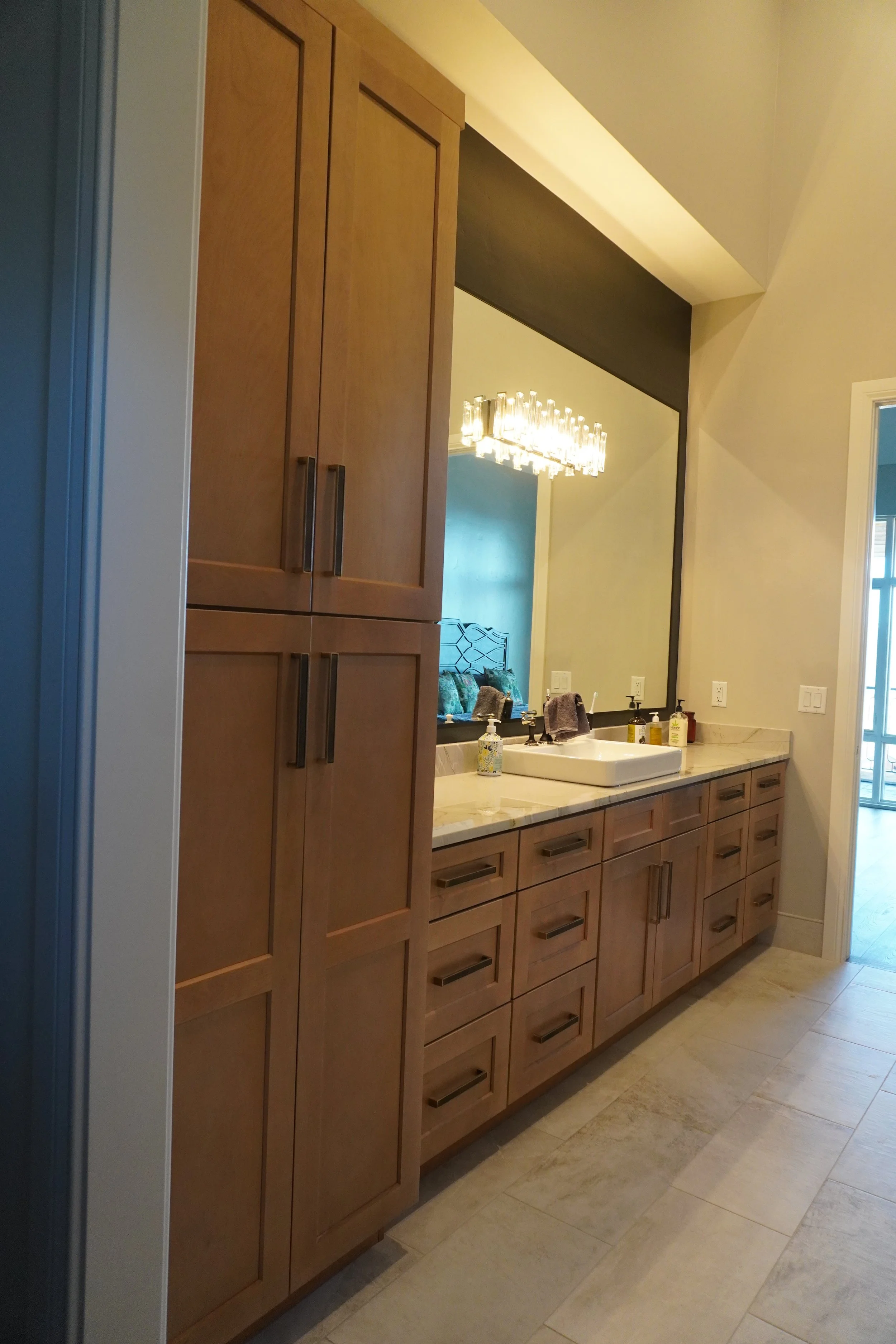 Bathroom vanity area with wooden cabinets, a large mirror, a vessel sink, and decorative items on the countertop.
