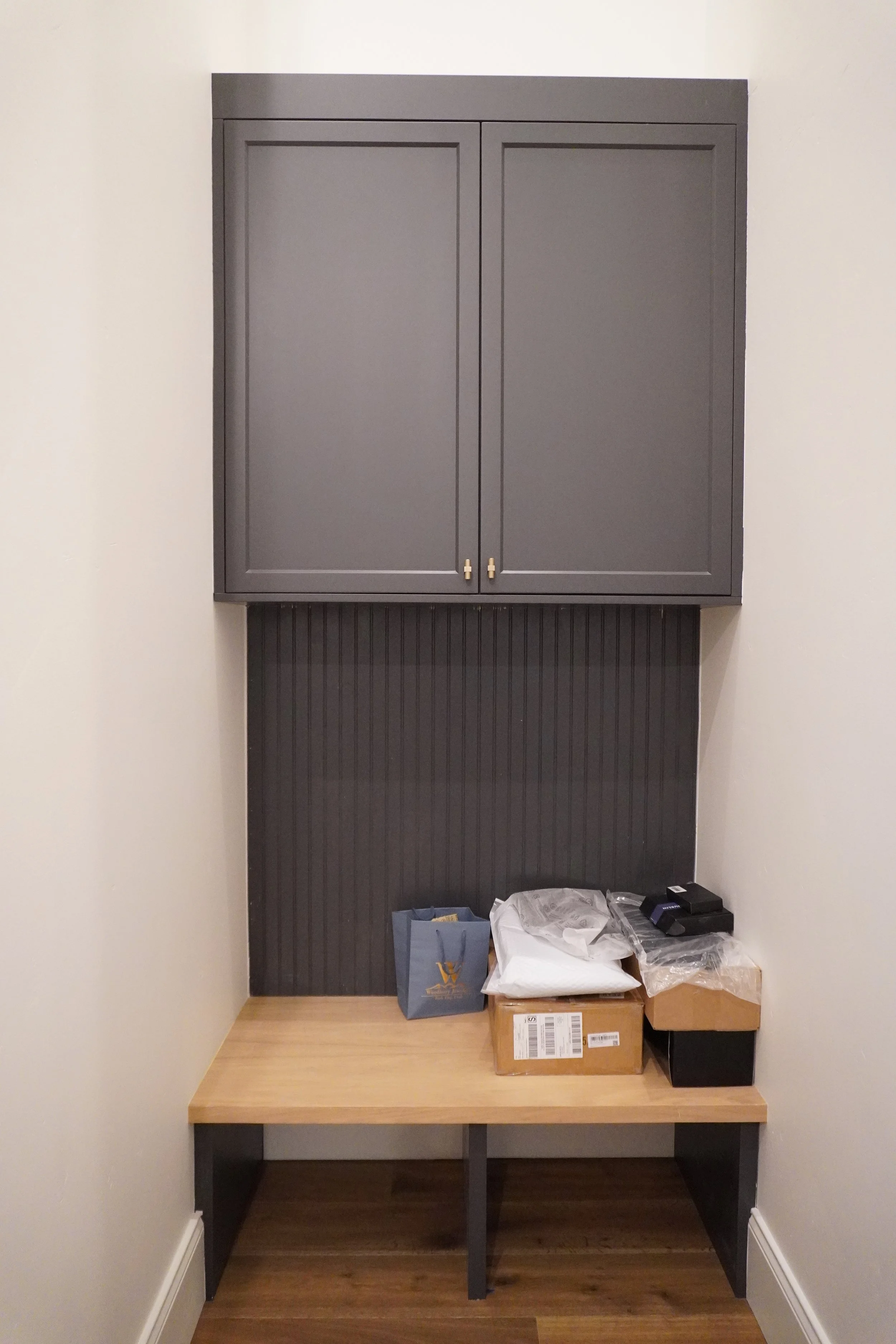 A small workspace with a wooden table, gray cabinets above, and various boxes and supplies on the table.