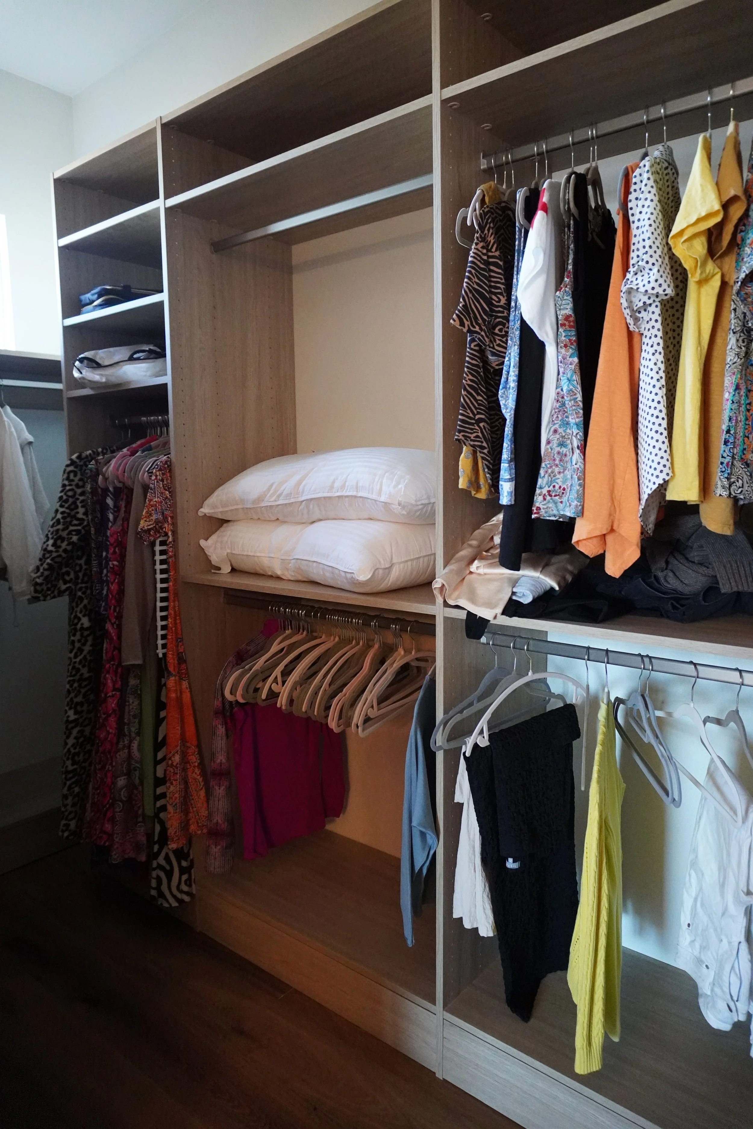 Open wardrobe with clothing, pillows, and folded clothes inside.