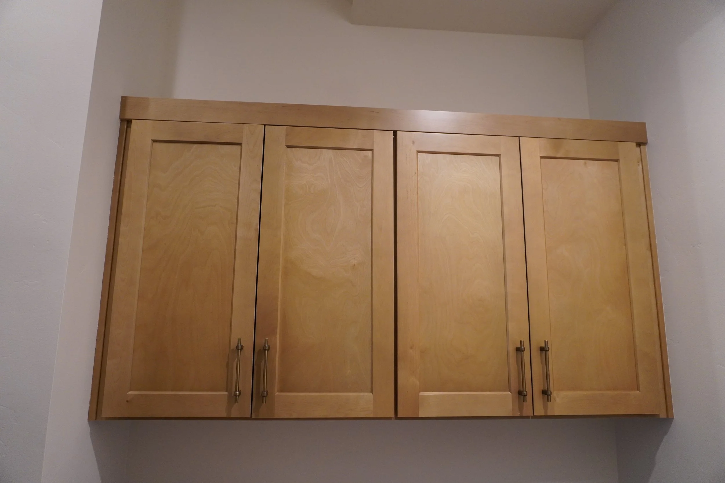 A wooden kitchen or bathroom wall cabinet with four doors and metal handles mounted on a white wall.