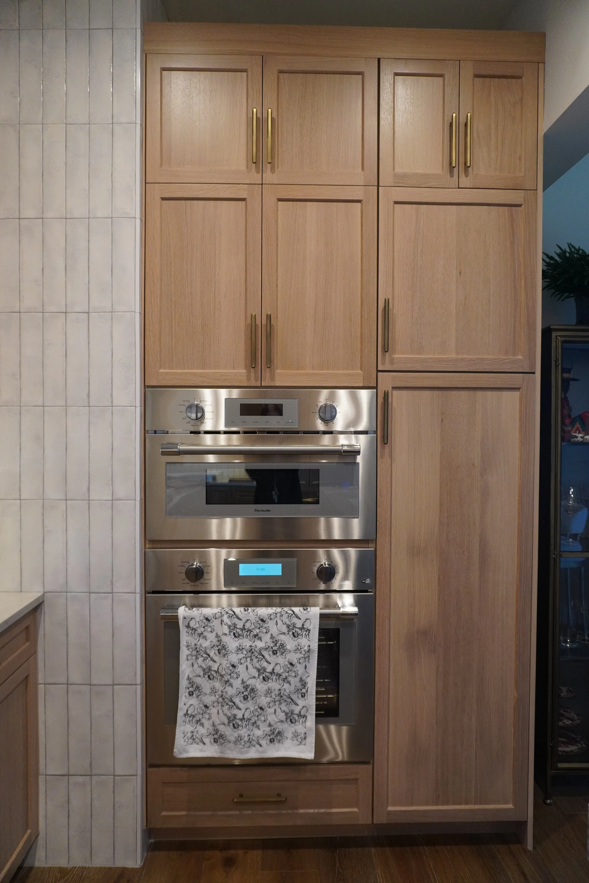 Kitchen wall with wooden cabinets and stainless steel oven, microwave, and warming drawer, with a towel hanging on the oven handle.