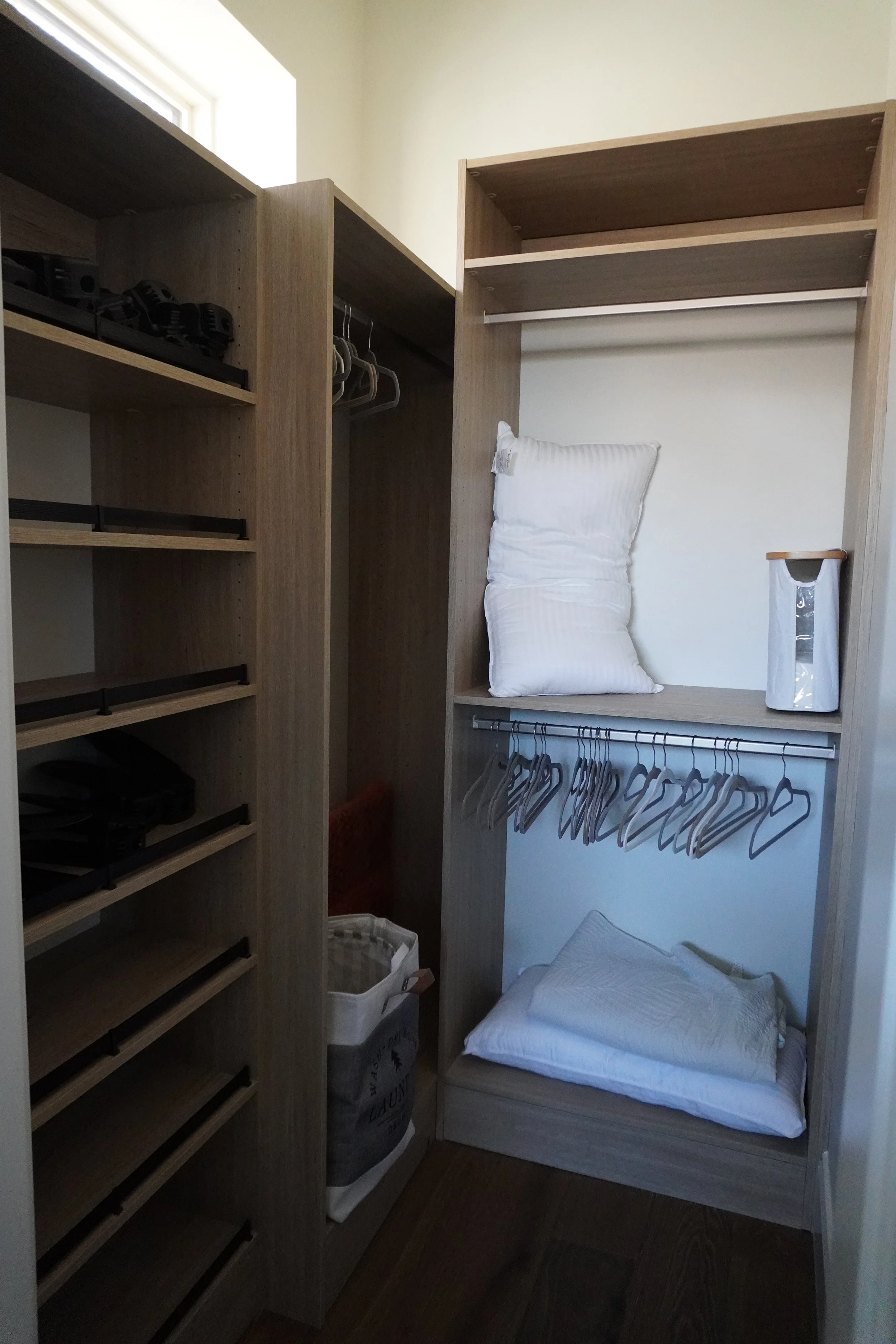 Empty closet with two shelves, a hanging rod with hangers, and a storage area with pillows and a trash can.