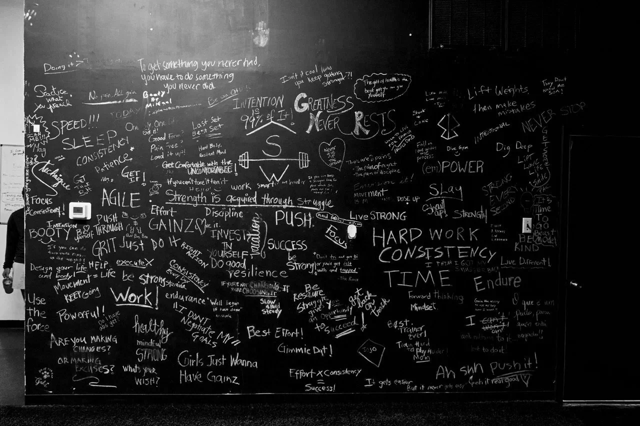 A black chalkboard covered with clients' intentions for their workouts about strength, perseverance, and success.