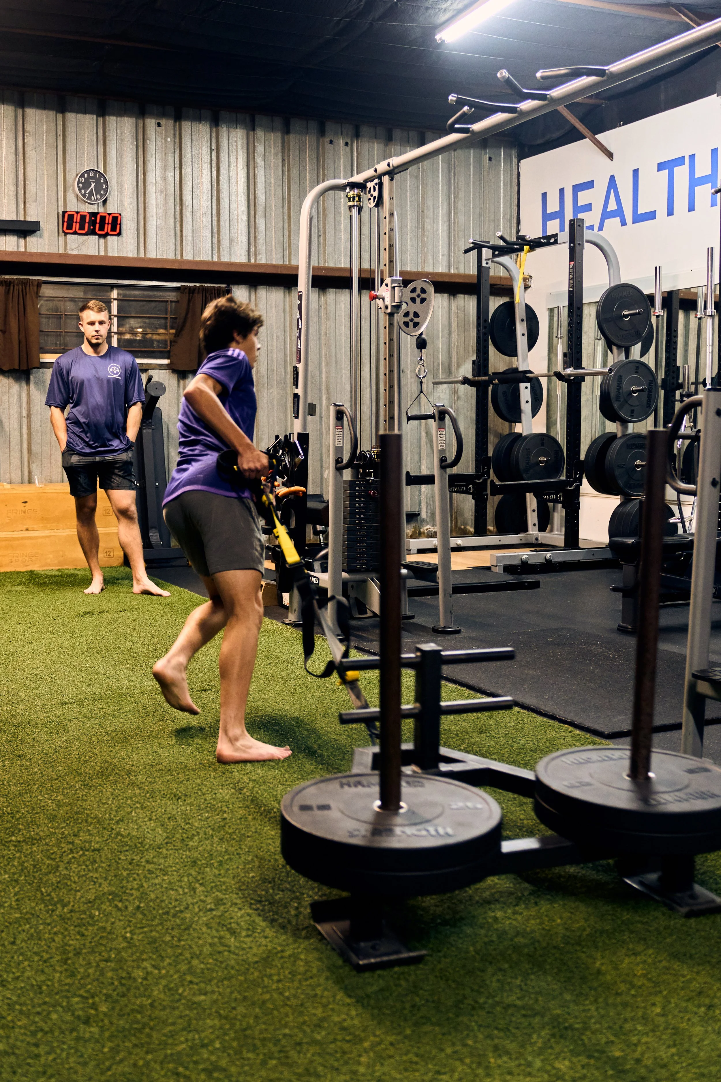 A client working out with a sled, while trainer observes them.