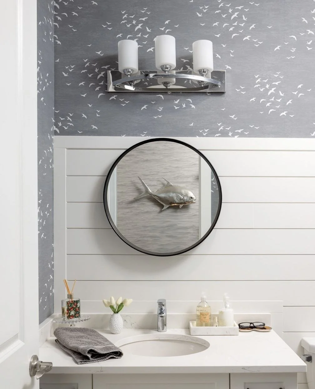 A unique art installation featuring a trio of fish sculptures is an unexpected delight in a previously awkward alcove of this lovely home on Bois Blanc Island. A coastal wallpaper depicting birds in flight was chosen for the powder room. The fish scu