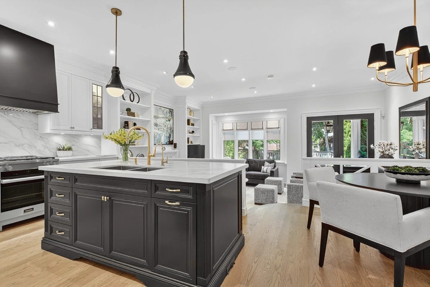 The bright, modern kitchen designed with white cabinetry is paired with a contrasting dark island, accented by warm brass hardware and fixtures for a stunning, dramatic look. Also perfect for entertaining, the streamlined cooking area features stainl