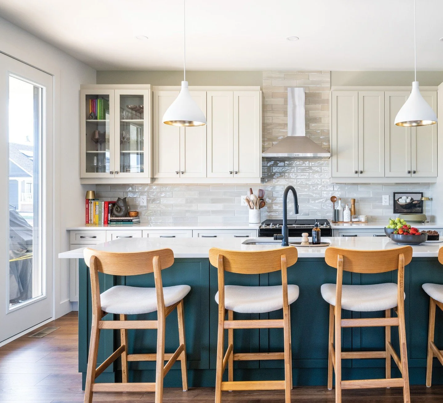 In this beautiful kitchen, the homeowners thoughtfully painted the wall in the same colour as the cabinets. Although they may not have chosen a green island, it fits into the overall design. The white pendants with a gold interior cast a soft glow ov