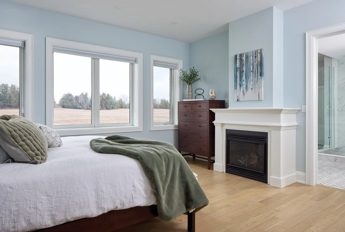 In a historic rural setting on the outskirts of Cambridge, where open fields and wide lawns shape a sense of calm possibility, a newly built home settles into place. The main-floor primary bedroom is a serene retreat, where a fireplace and sweeping v
