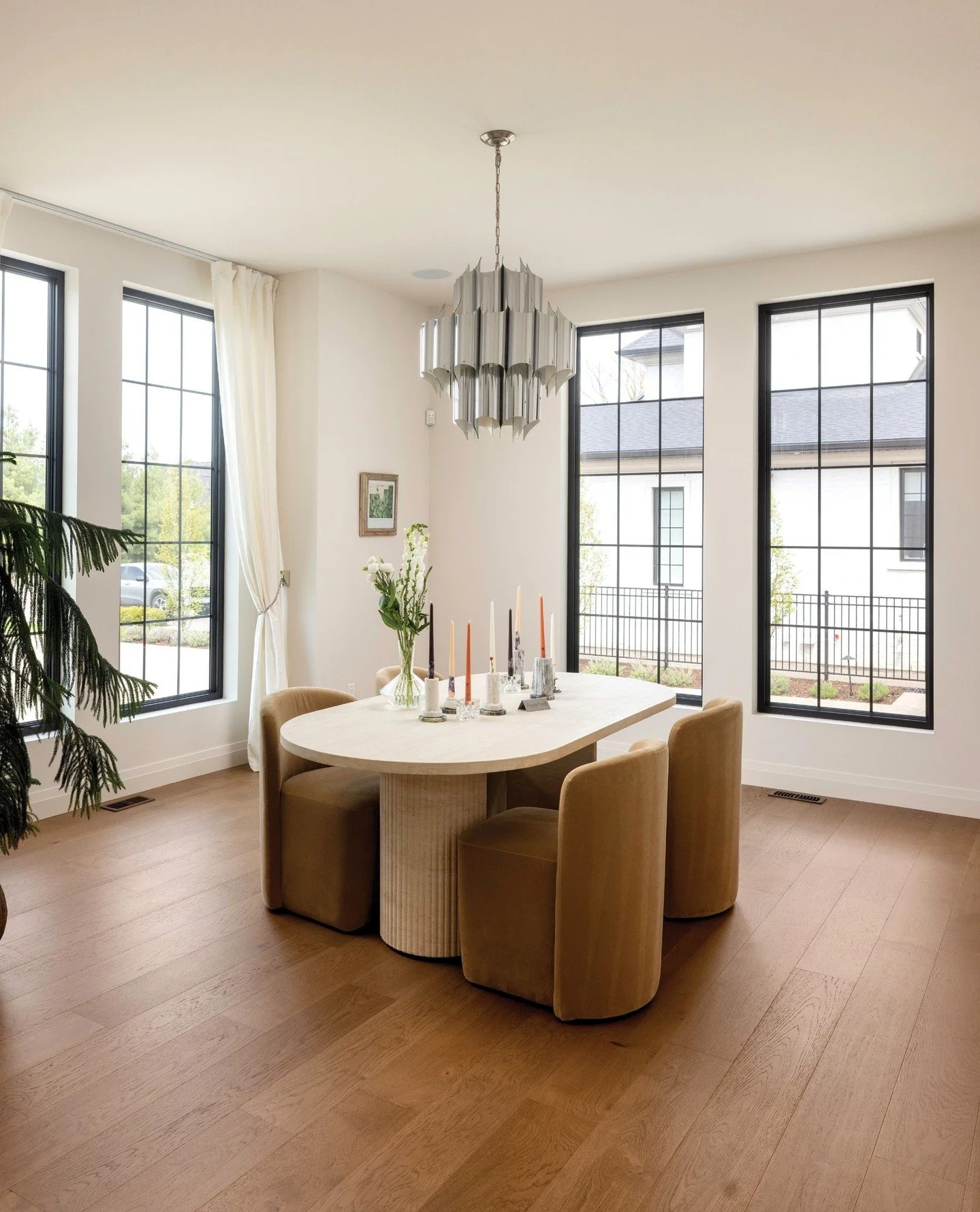 A modern, yet welcoming space for entertaining in this dining room. The  sculptural chandelier and curved dining furniture introduce softness to the bright dining area. Black-framed windows contrast beautifully with the home&rsquo;s warm palette. See