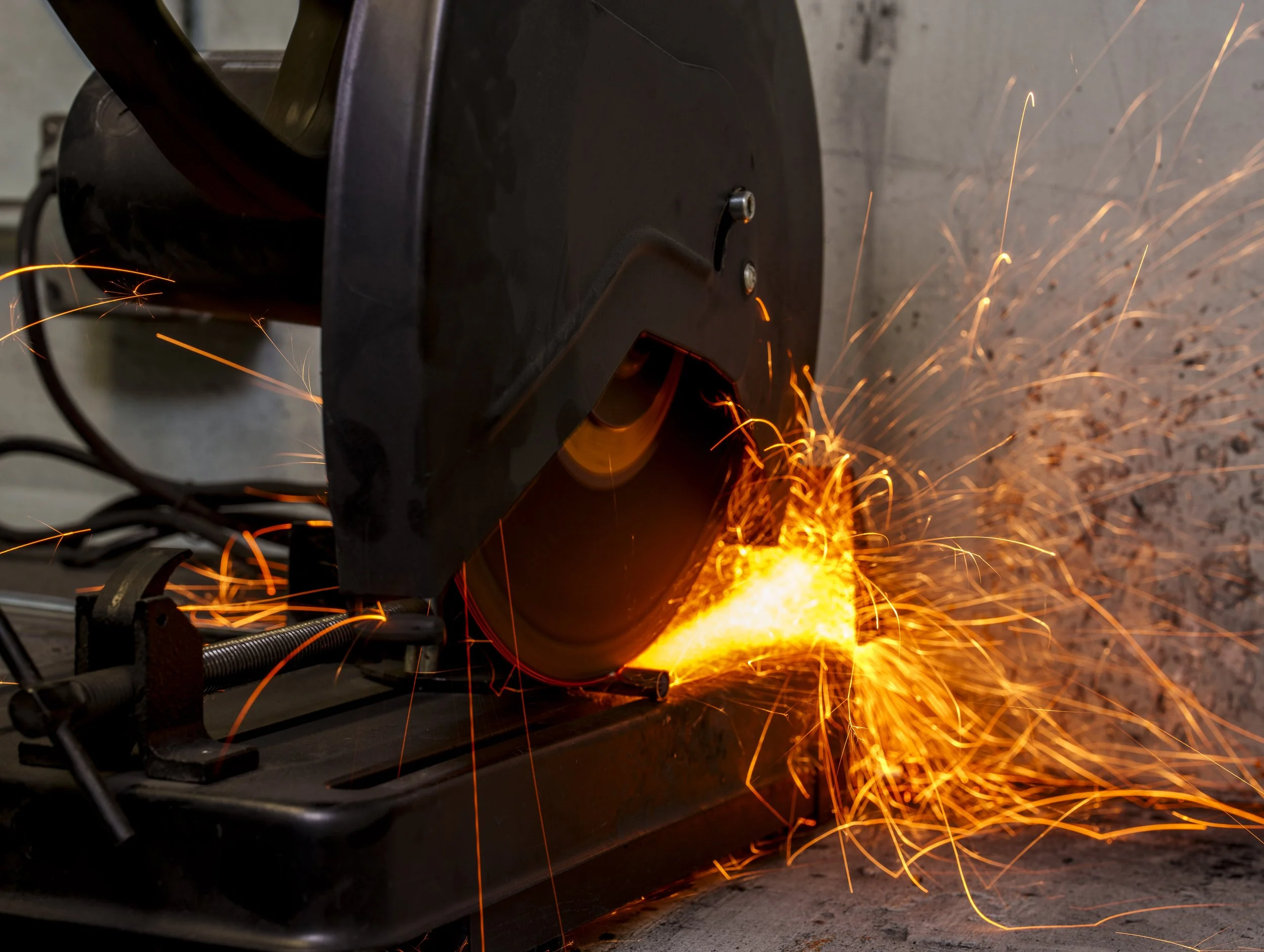 A welding machine emitting bright sparks while welding metal, with a concrete wall background.