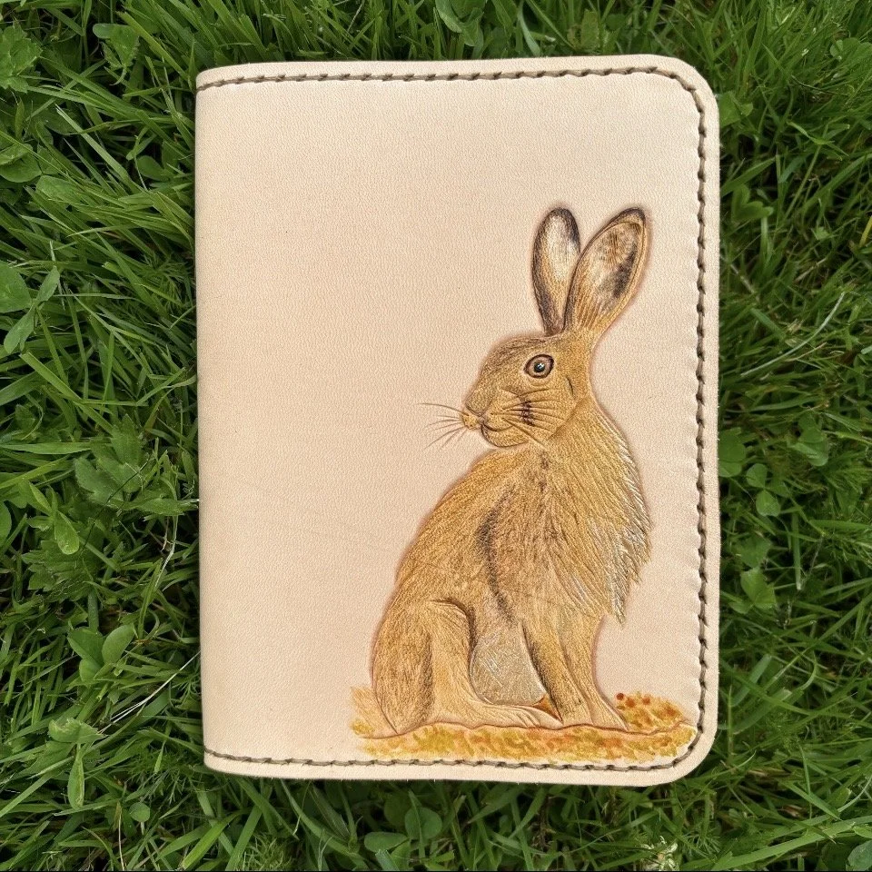 Wild Hare A6 Colour added.jpgWild Hare A6 beside A5.jpg Leather handcrafted journal cover features brown hare on green grassy background. In colour on natural leather.
