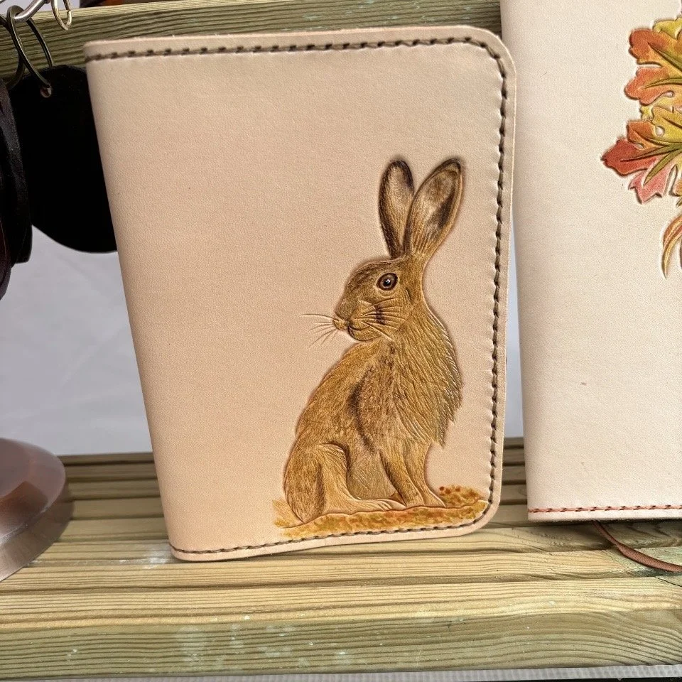 Wild Hare A6 beside A5.jpg Leather handcrafted journal cover features golden brown hare looking left. In colour on natural leather. Beside A5 journal showing size difference.