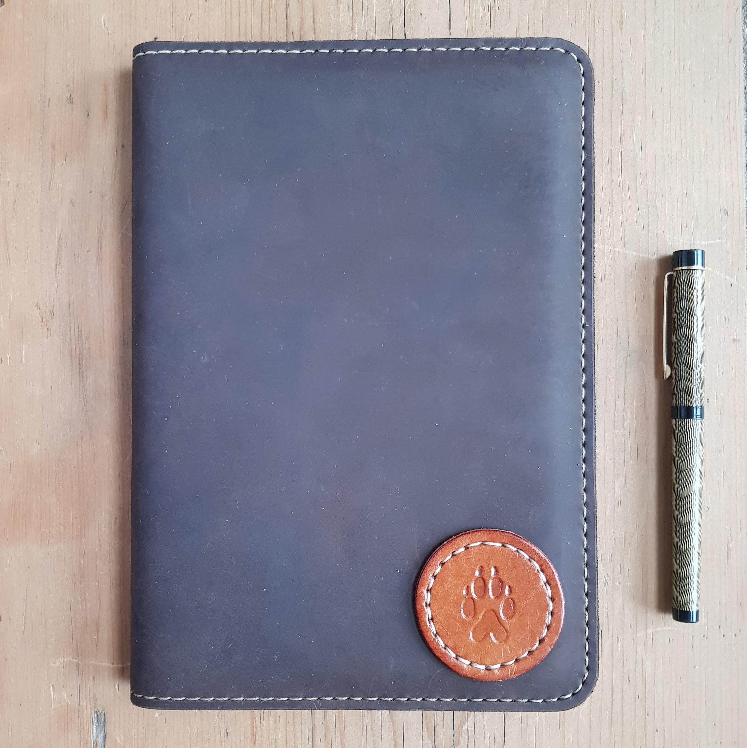 Paw Print Patch on Oiled Leather A5.jpg Brown oiled vegetable tanned leather featuring a tan patch  with a wolf or dog paw print.