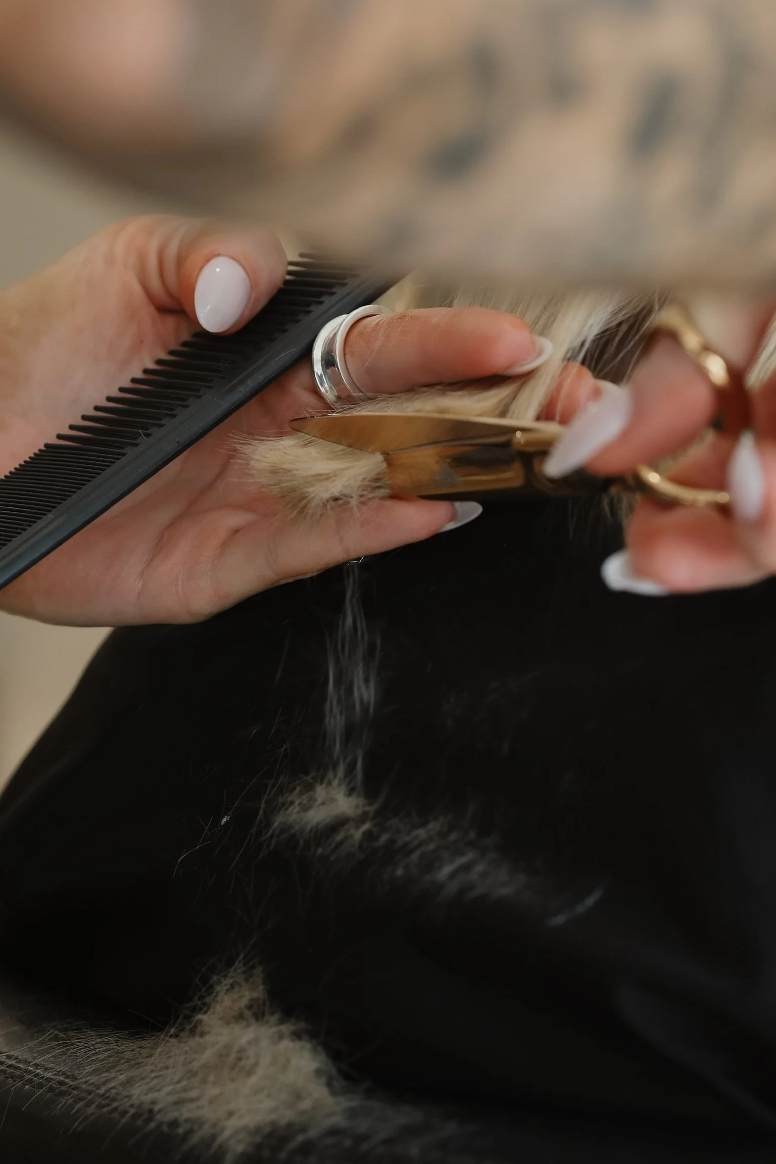 A hairstylist is cutting a woman's long, wet brown hair with scissors, holding a wide-tooth comb in her other hand in a salon.