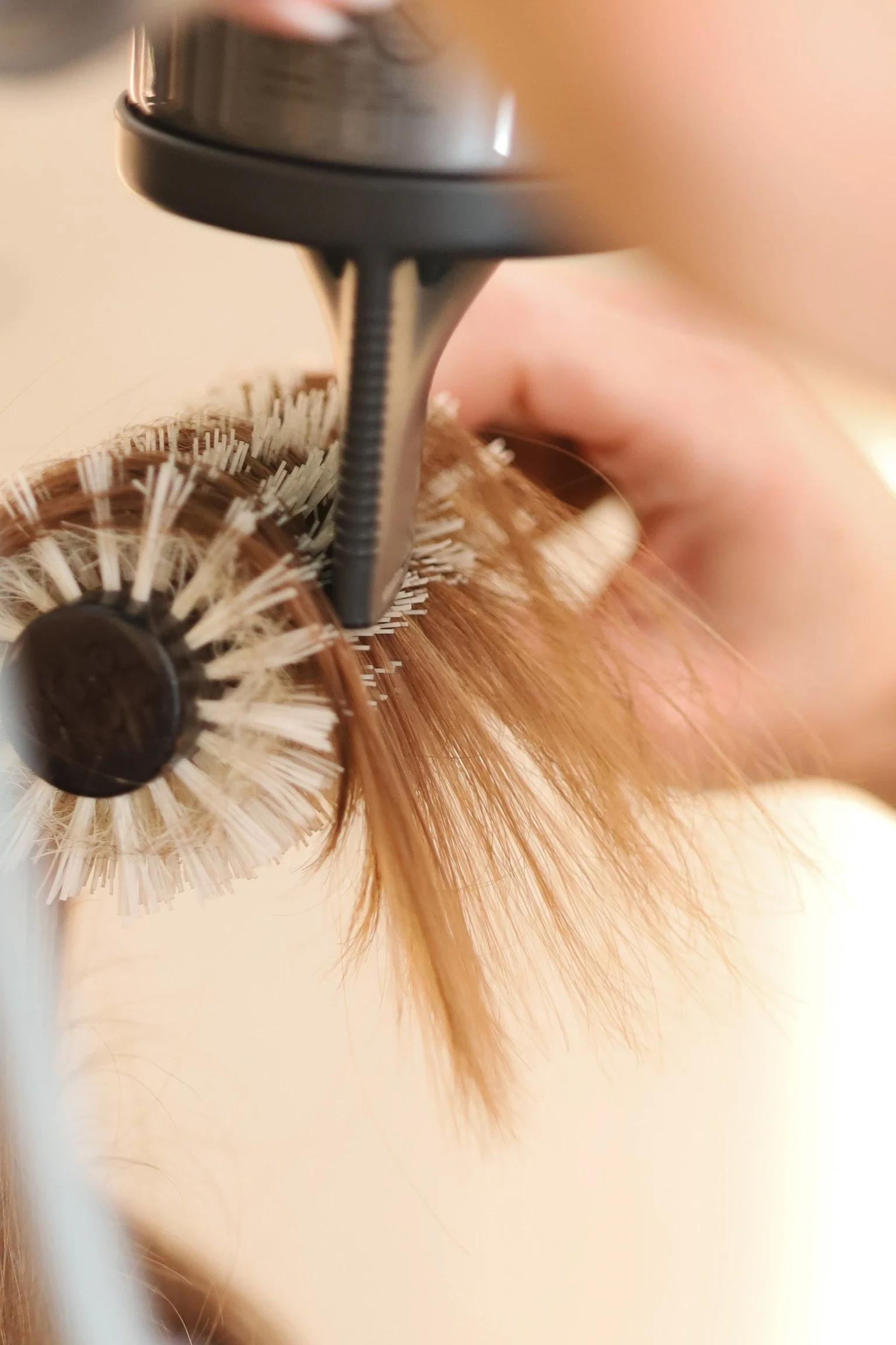 A hairstylist blow-drying a woman's long blonde hair in a salon.