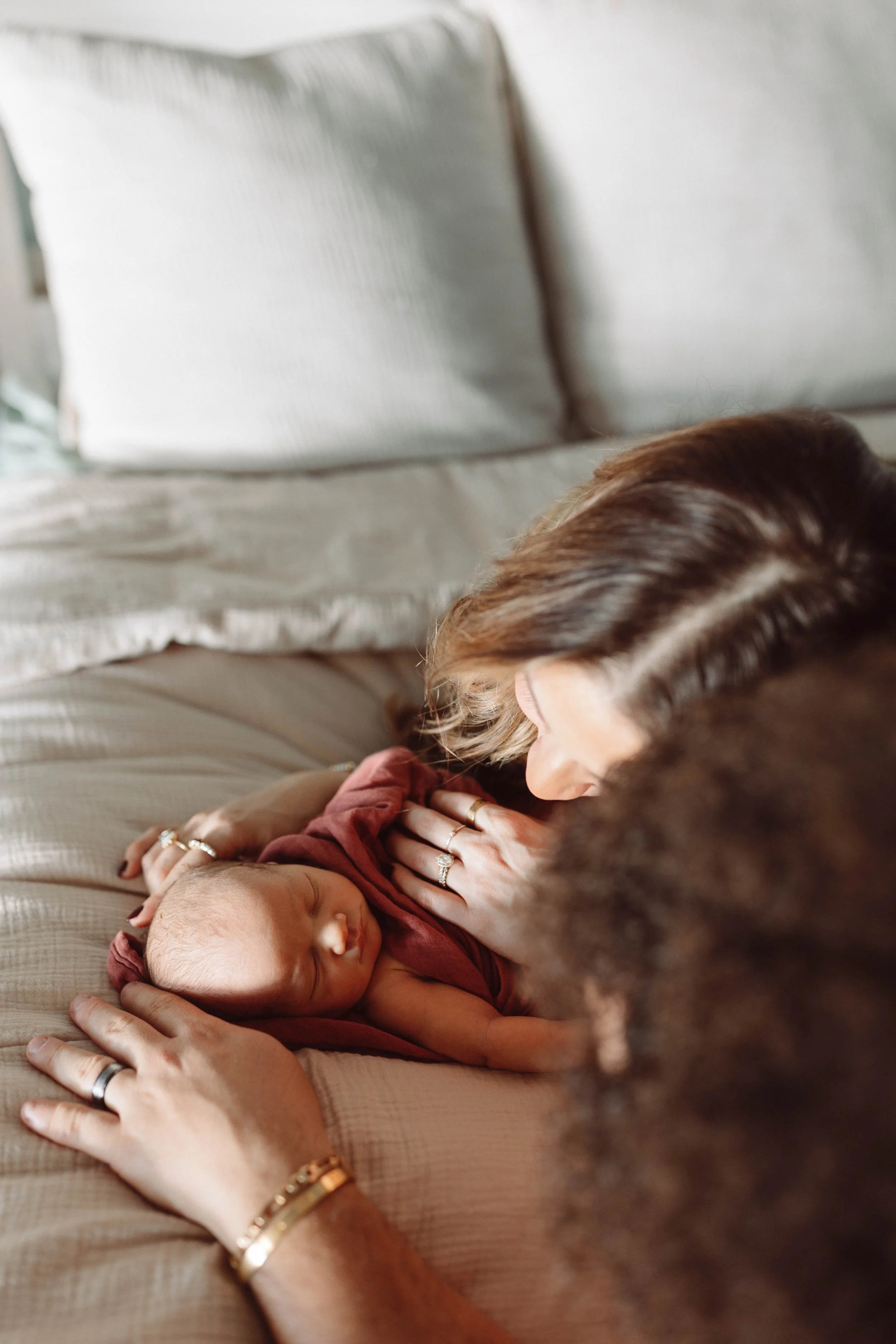 man and woman lay on bed snuggling newborn baby wrapped in pink swaddle