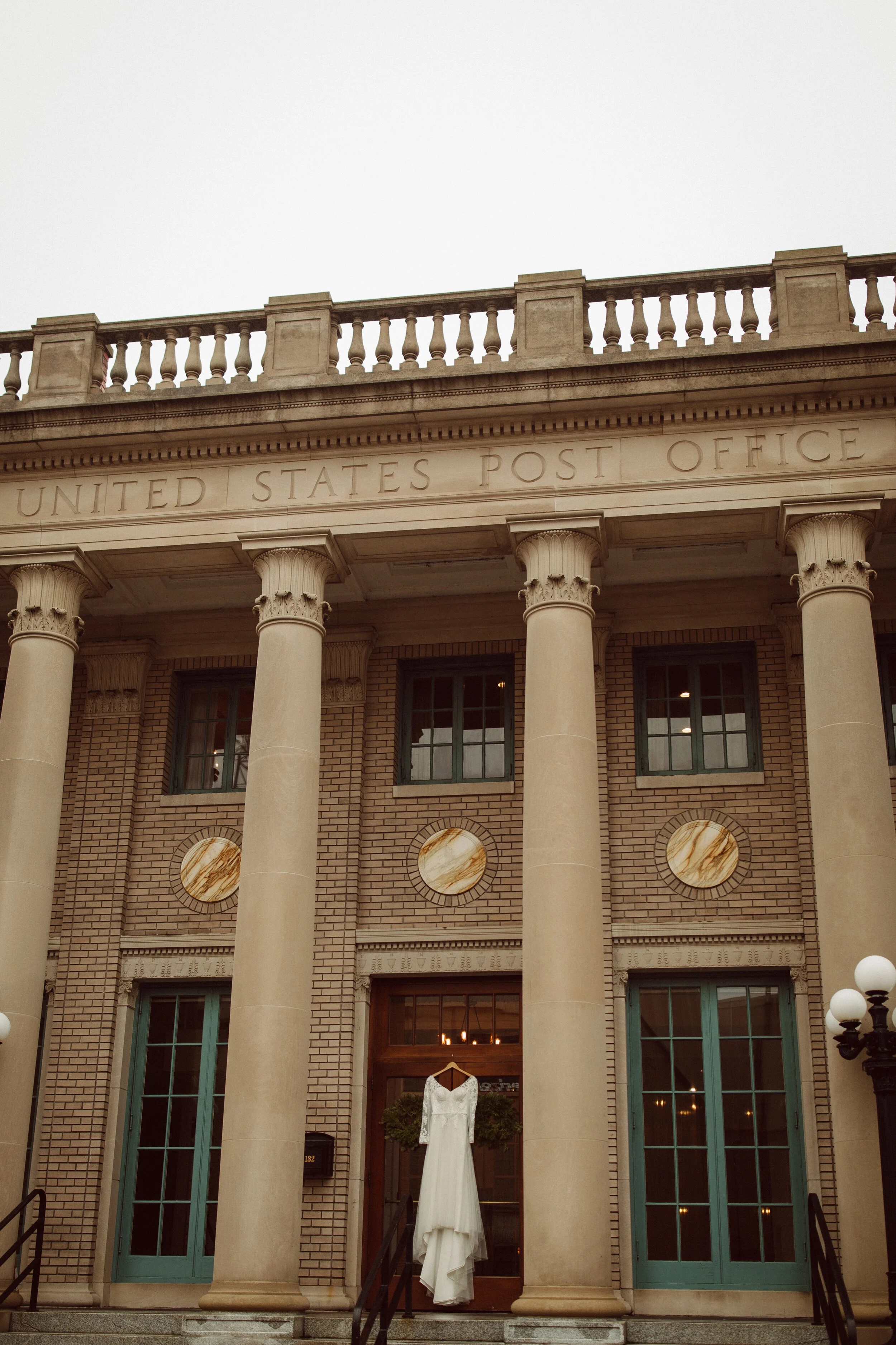 A white dress hanging outside a historic post office building with large columns and brick facade.