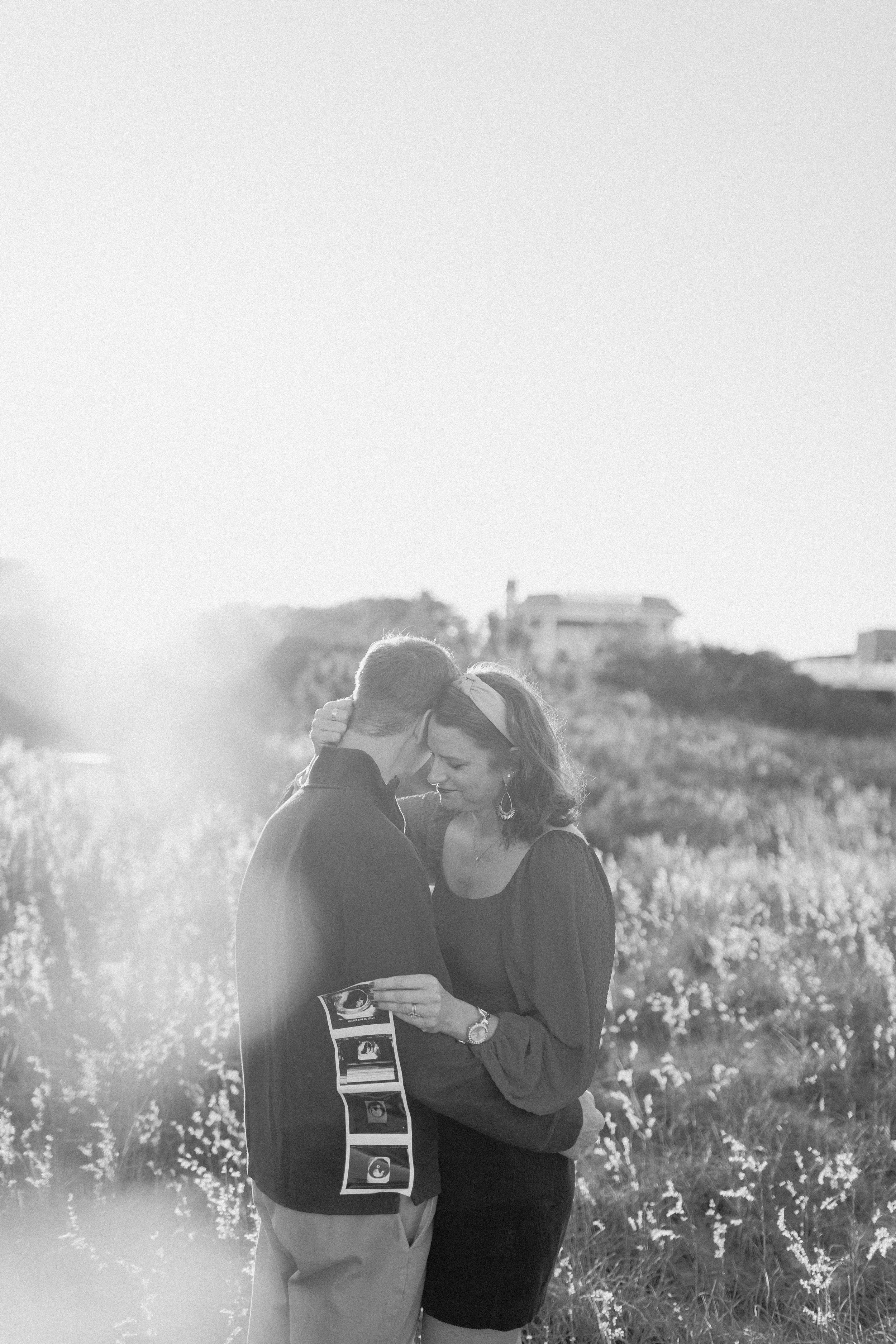 virginia beach navy couple holds miracle baby onesie standing at virginia beach north end