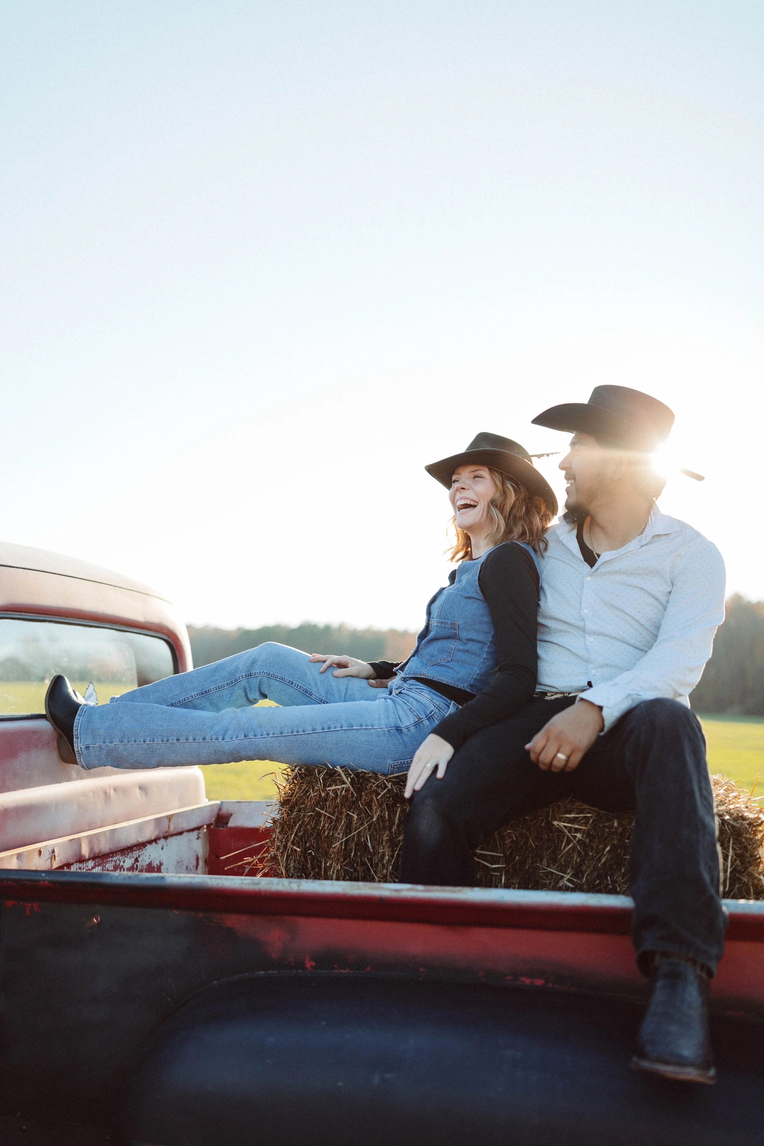 couple walks through field wearing cowboy hats and western wear 