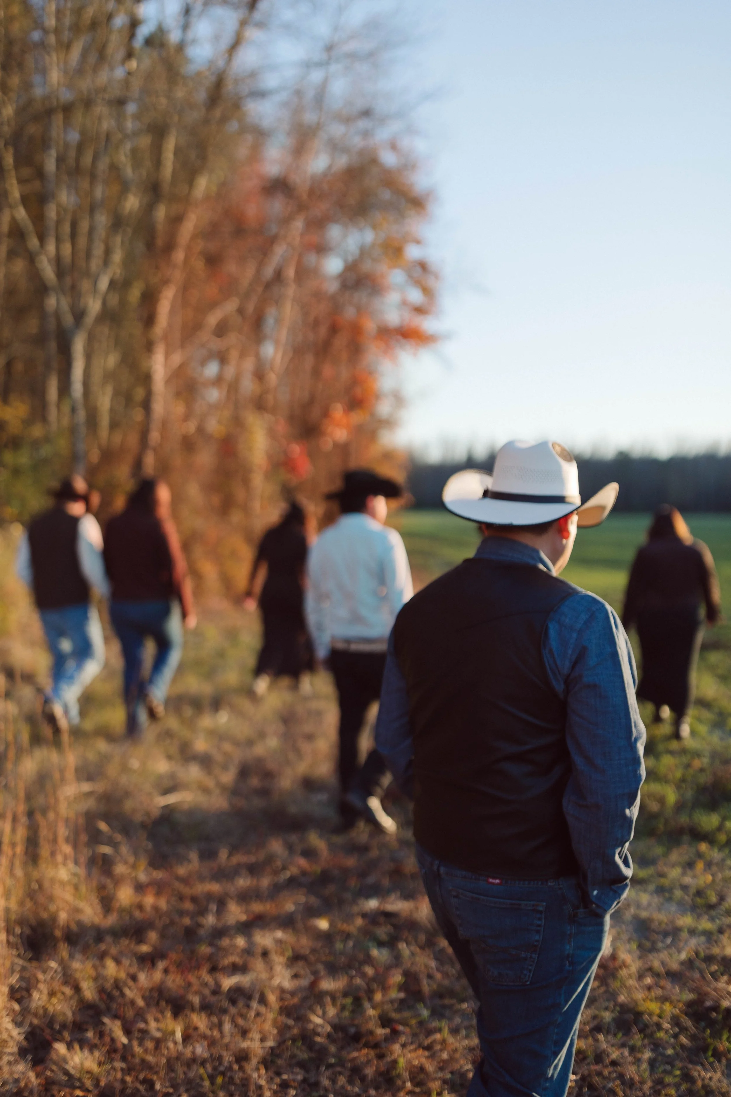 family walks away from camera toward treeline 