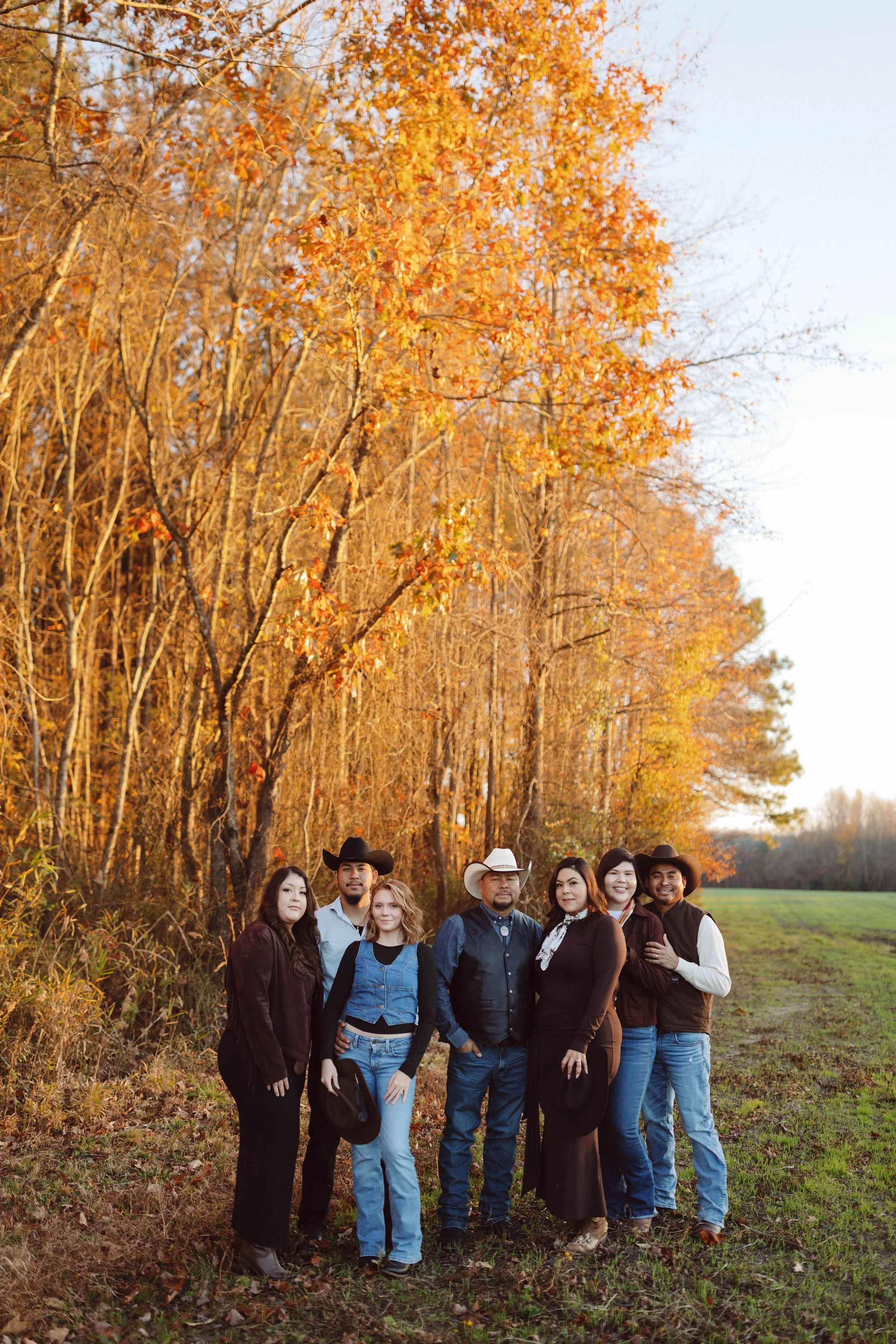 large family gathers under fall foliage in a field wearing western attire