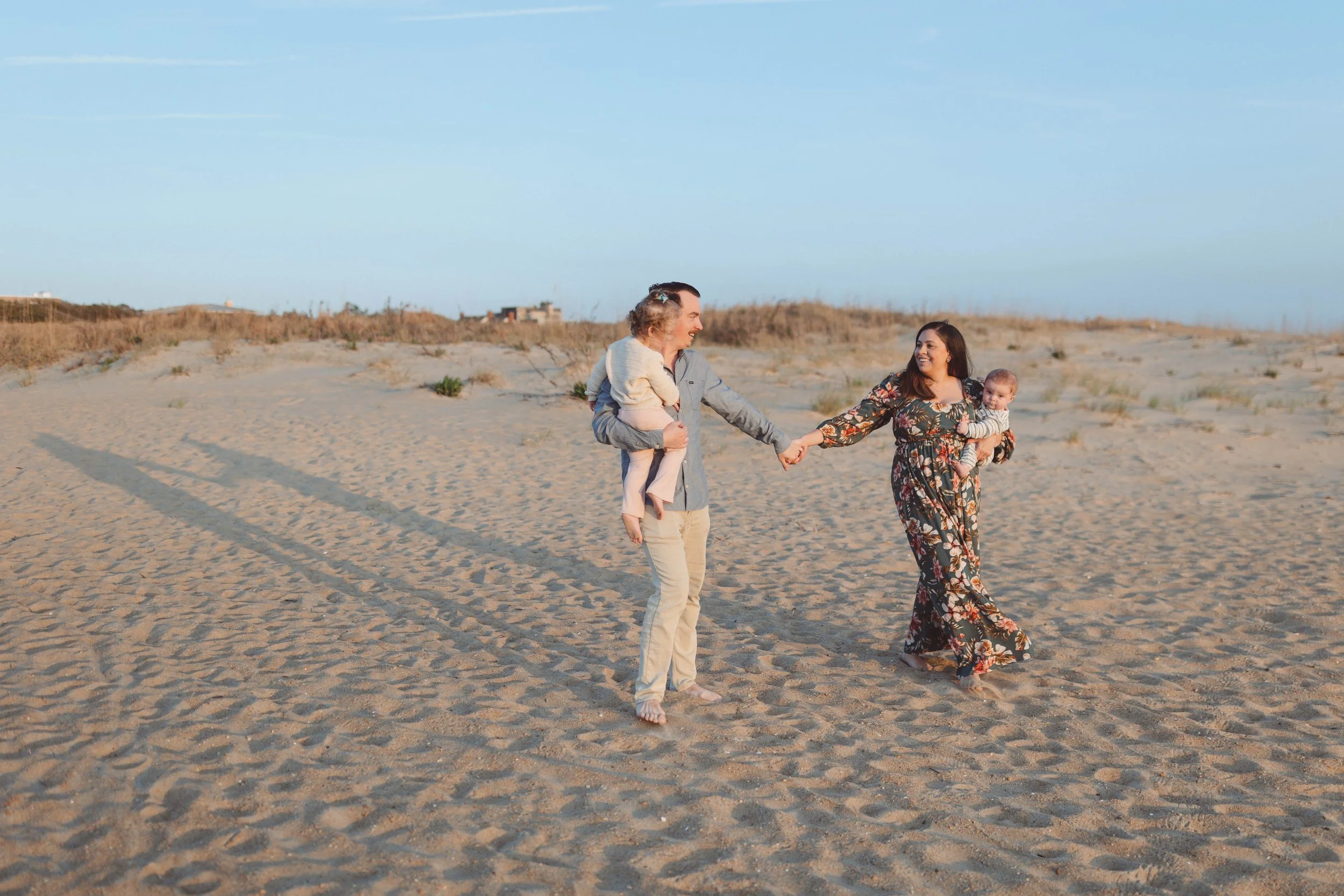 family walking down beach holding hands smiling and looking at children